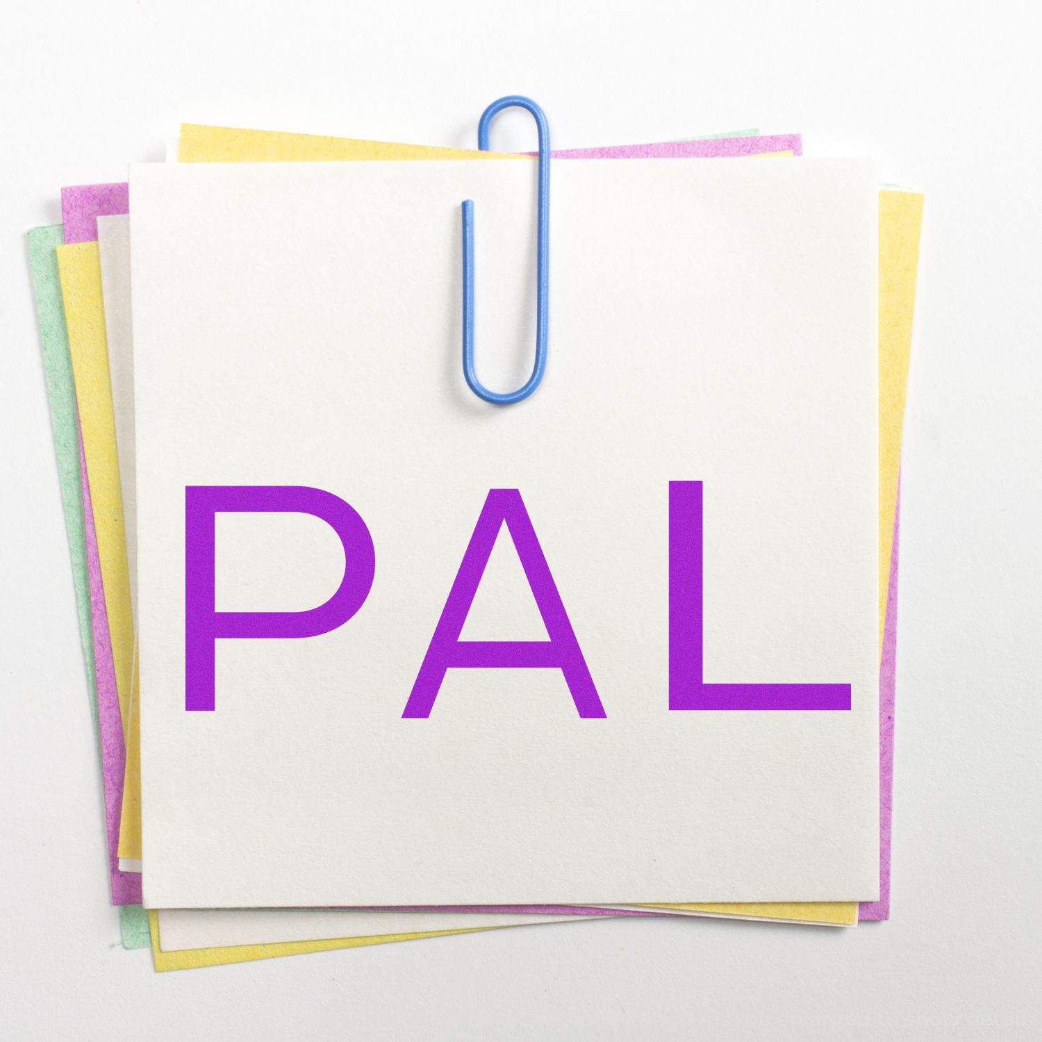 Large PAL Rubber Stamp imprint on a stack of colorful sticky notes, held together by a blue paperclip on a white background.