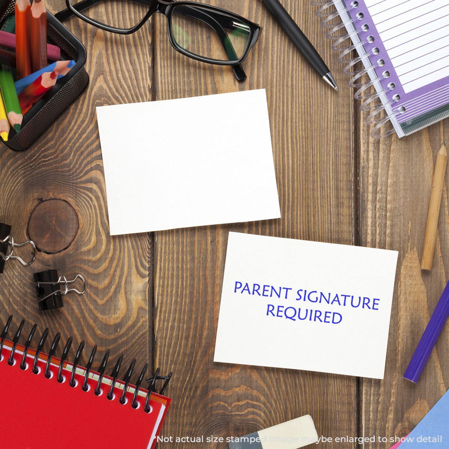 Large Parent Signature Required Rubber Stamp used on a white card, surrounded by office supplies on a wooden desk.