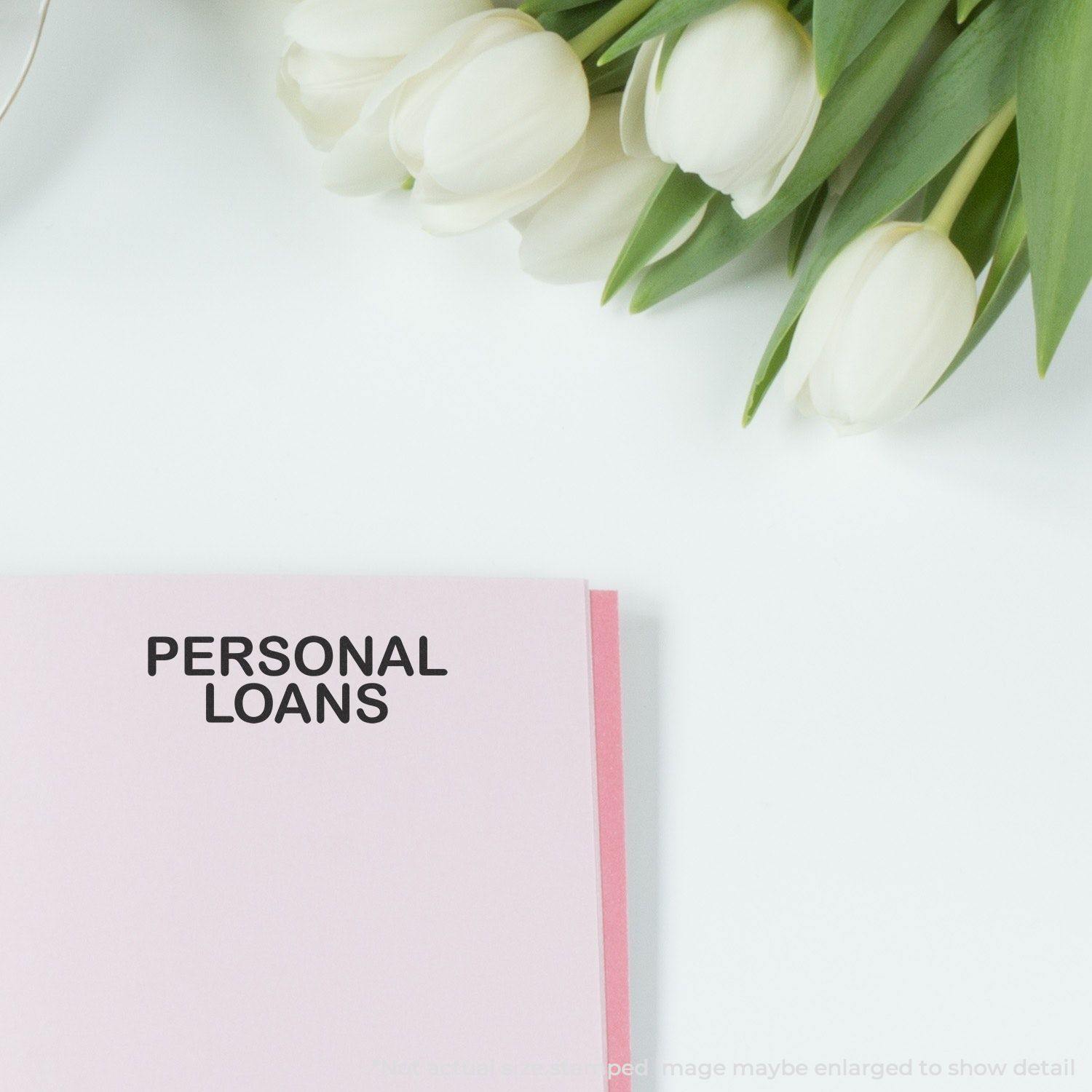 A pink document stamped with PERSONAL LOANS using the Large Personal Loans Rubber Stamp, placed next to white tulips on a white surface.