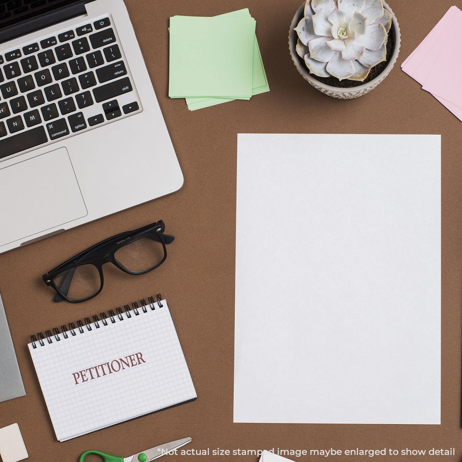 Desk with a Slim Pre-Inked Petitioner Stamp, glasses, notepad, laptop, succulent, and blank paper.