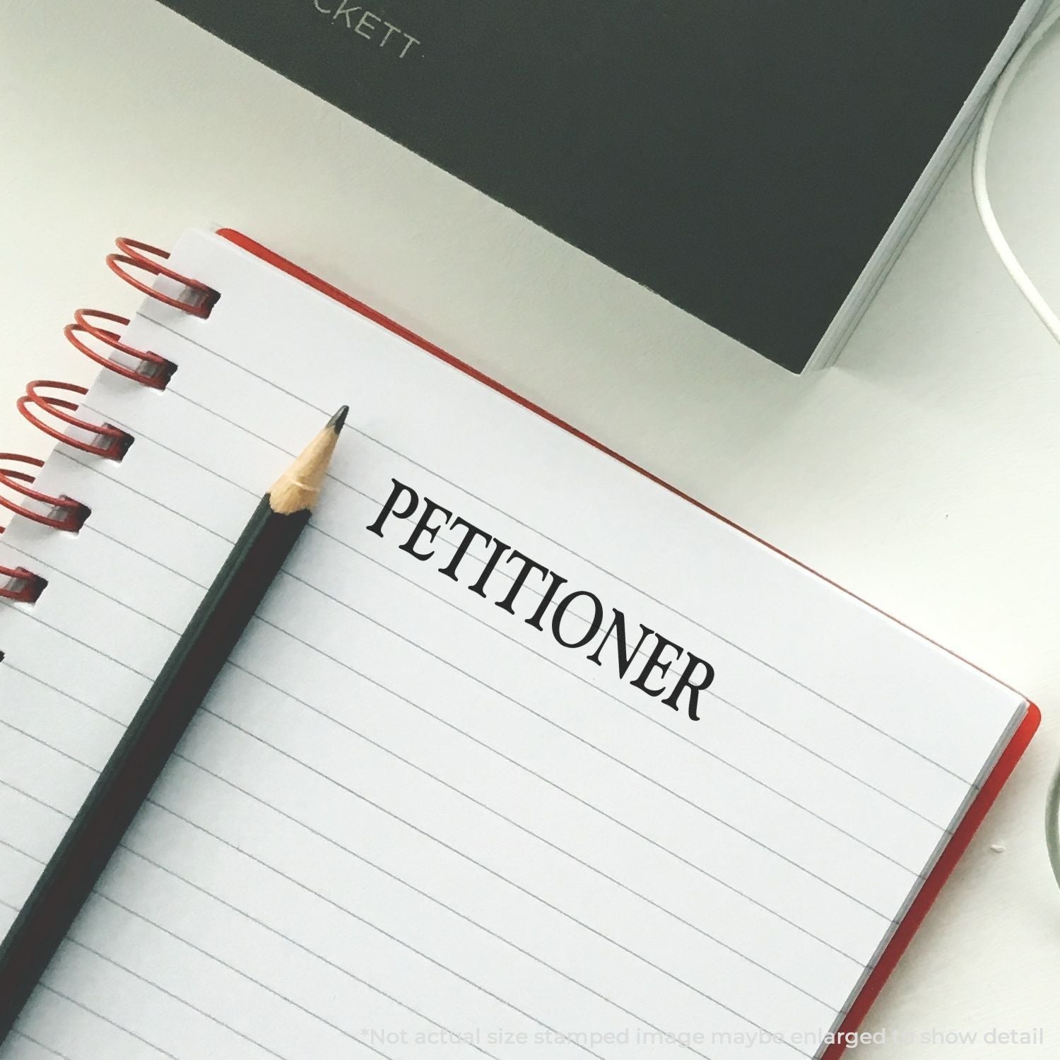 Self Inking Petitioner Stamp used on a lined notebook page with a pencil beside it.