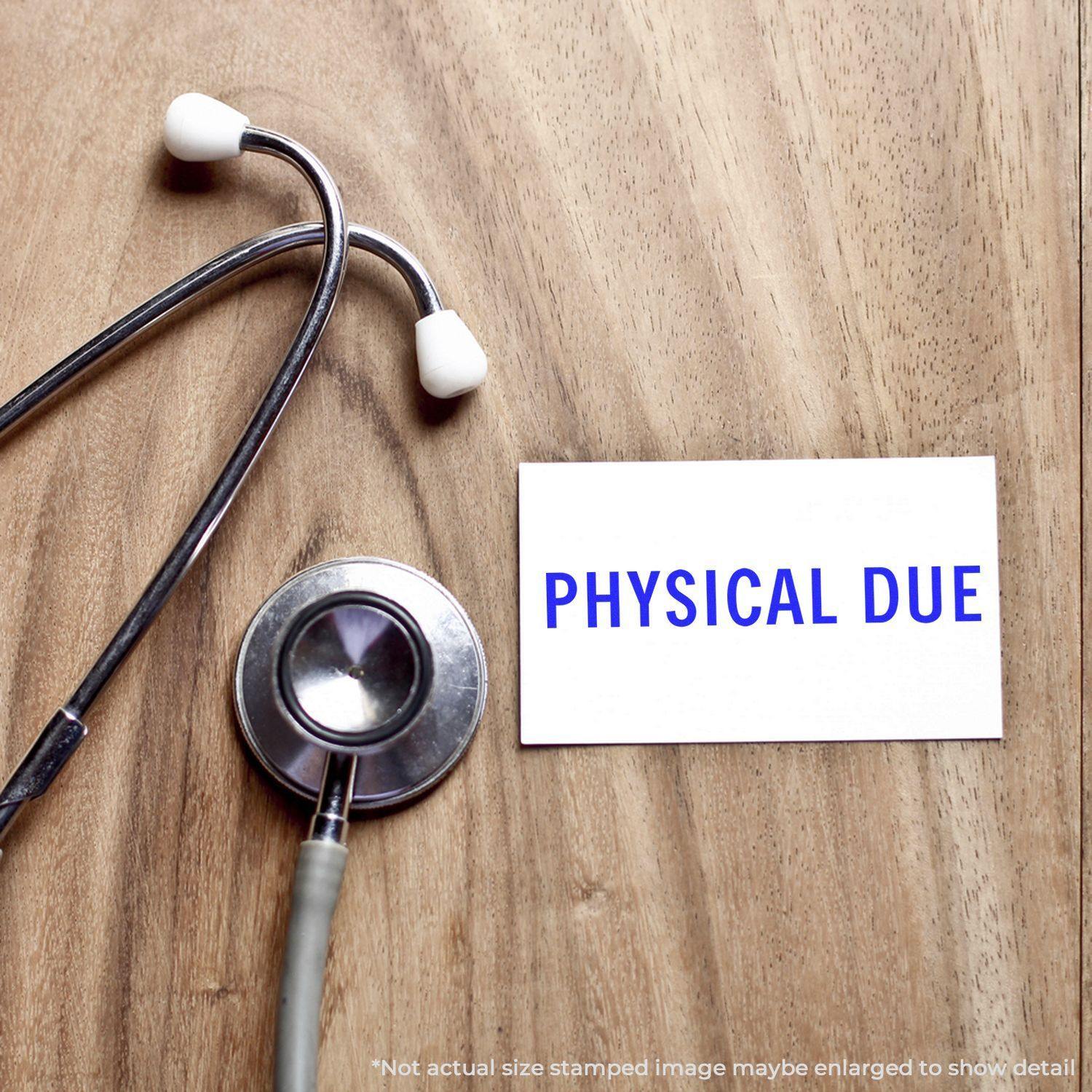 Stethoscope on wooden surface next to a card stamped with PHYSICAL DUE in blue, indicating a reminder for a physical check-up.