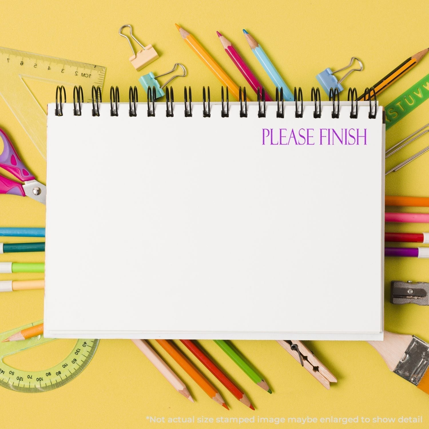 A blank notebook page stamped with PLEASE FINISH using the Self Inking Please Finish Stamp, surrounded by colorful stationery on a yellow background.