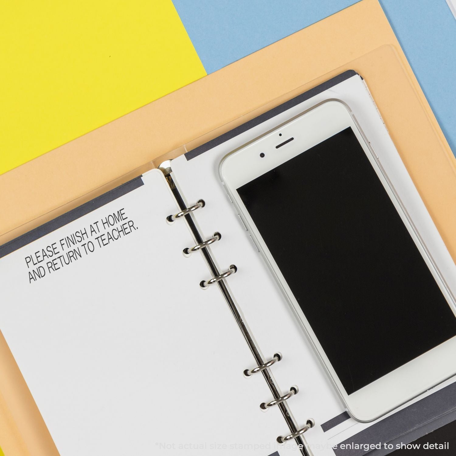 A binder with a stamped message PLEASE FINISH AT HOME AND RETURN TO TEACHER using the Self Inking Please Finish At Home Stamp, next to a smartphone.