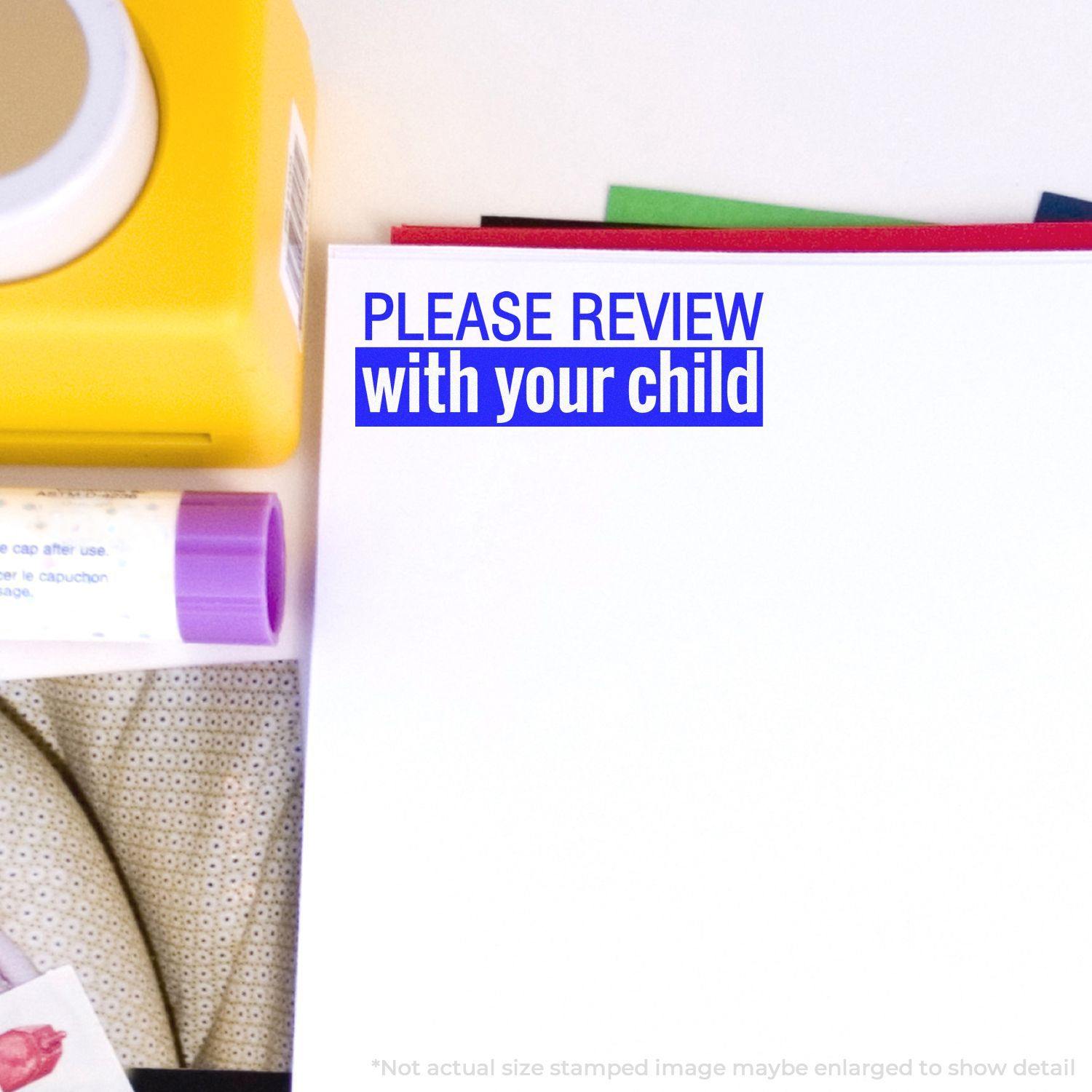 Large Please Review with your child Rubber Stamp in use on white paper, surrounded by a yellow stamp, glue stick, and colorful papers.