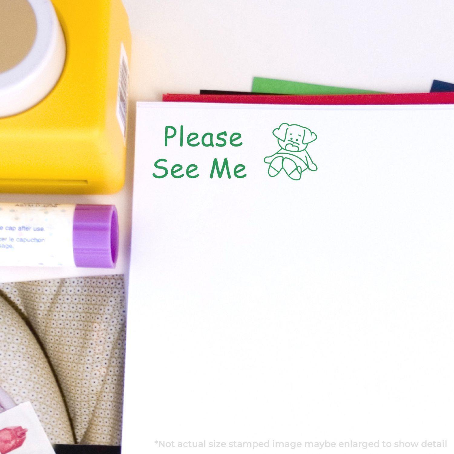 Large Self Inking Please See Me Stamp in green ink on white paper, surrounded by office supplies including a yellow container and a purple marker.