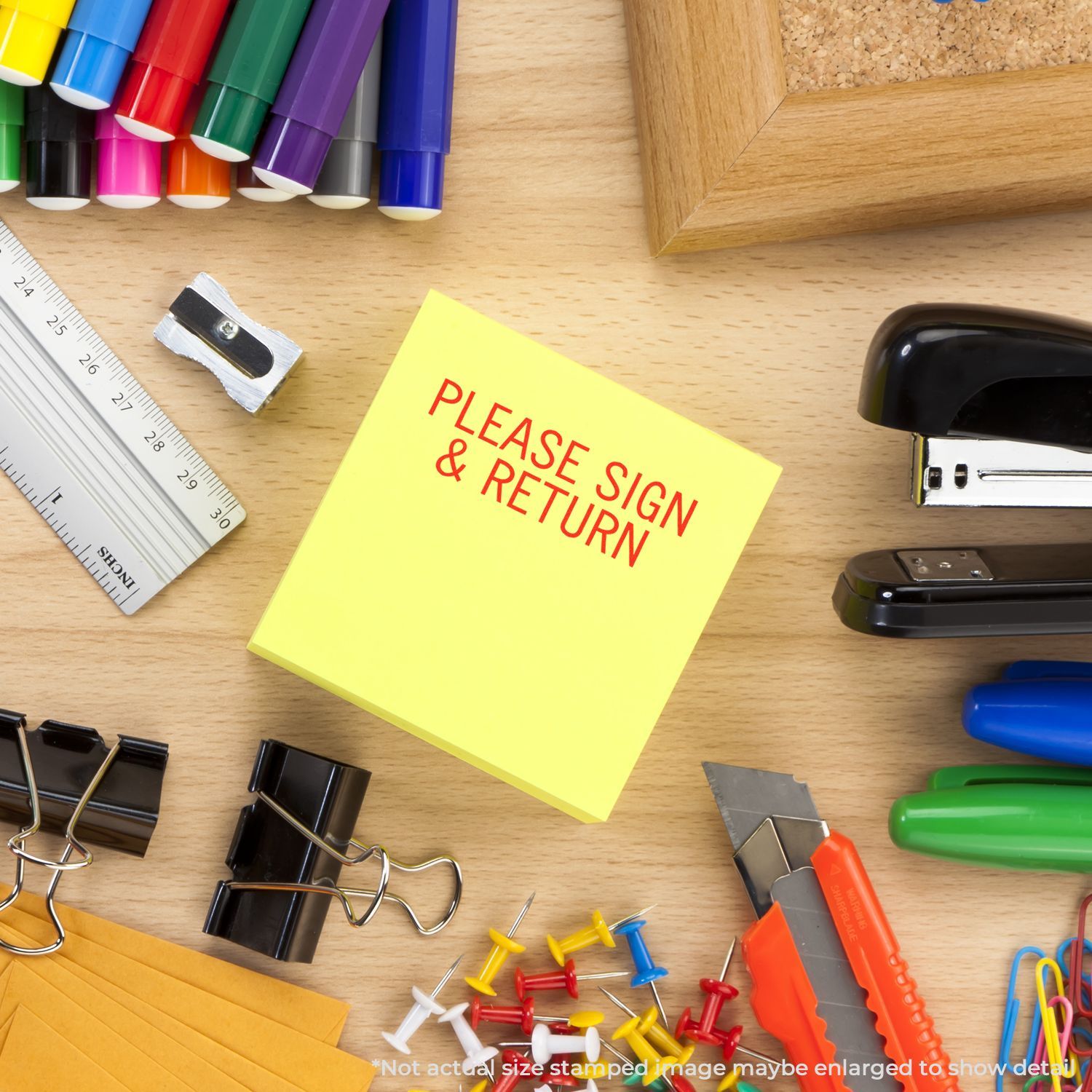 Desk with office supplies including a Self Inking Please Sign Return Stamp on a yellow sticky note, surrounded by pens, stapler, and push pins.