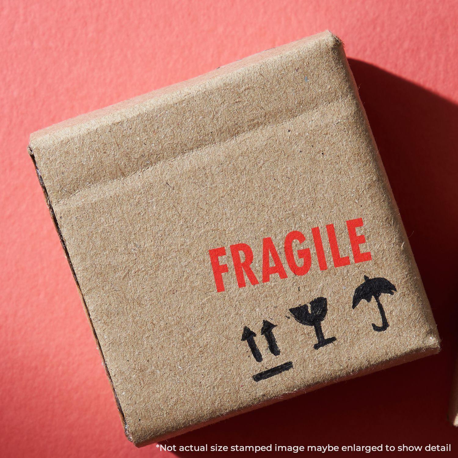 A cardboard box stamped with FRAGILE using a Large Pre-Inked Fragile Stamp, placed on a red background.