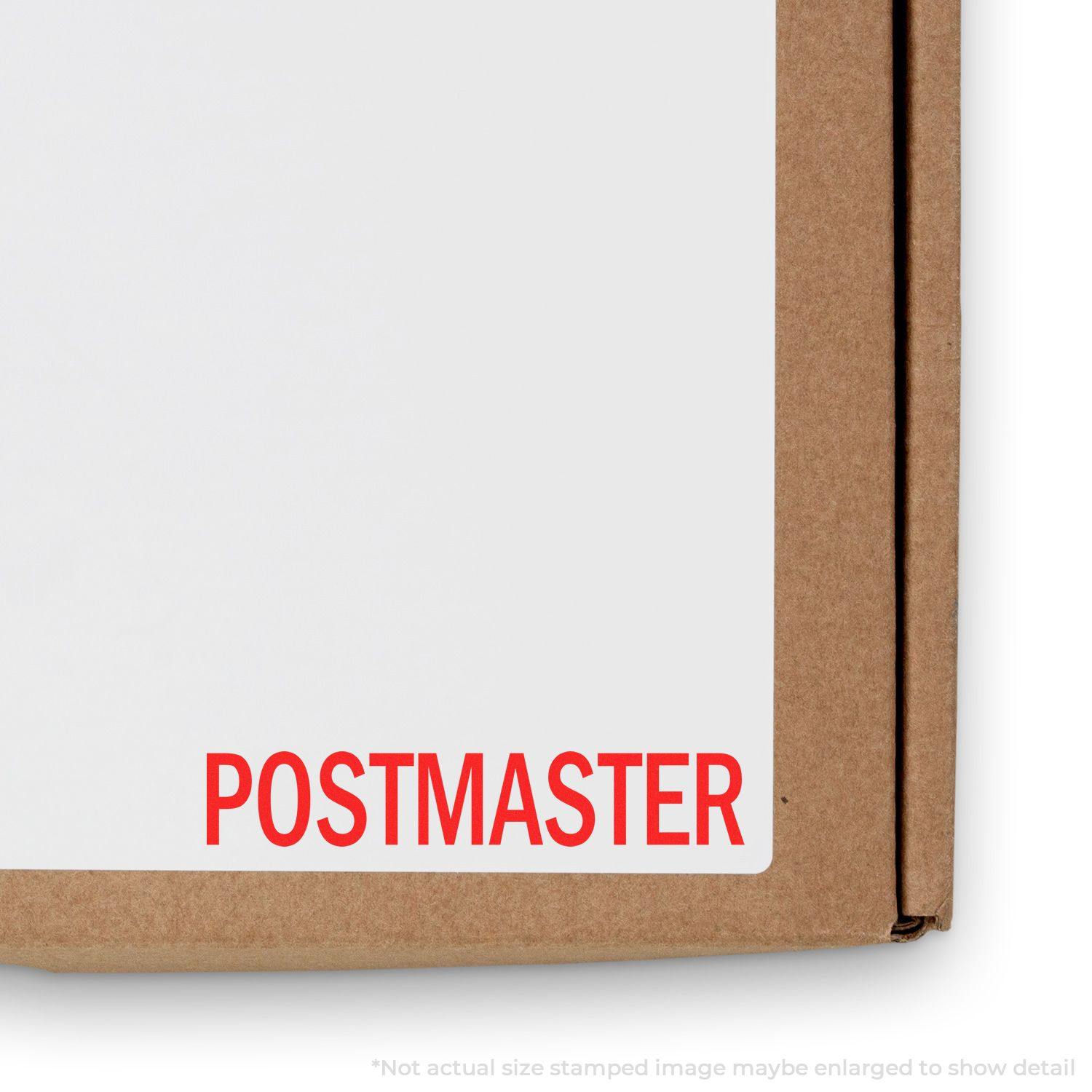 The POSTMASTER stamped image (from Postmaster Rubber Stamp) in red ink on a white paper attached to a brown cardboard box.