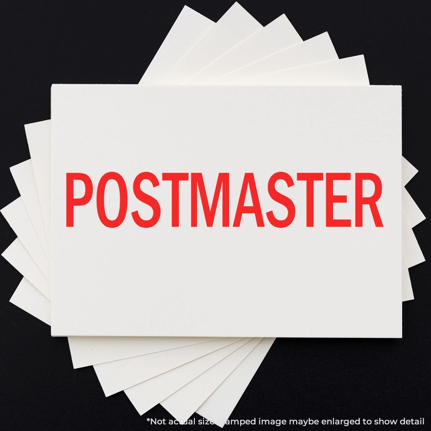 A word POSTMASTER (stamped from Postmaster Rubber Stamp) in red ink on white paper, with multiple sheets underneath.