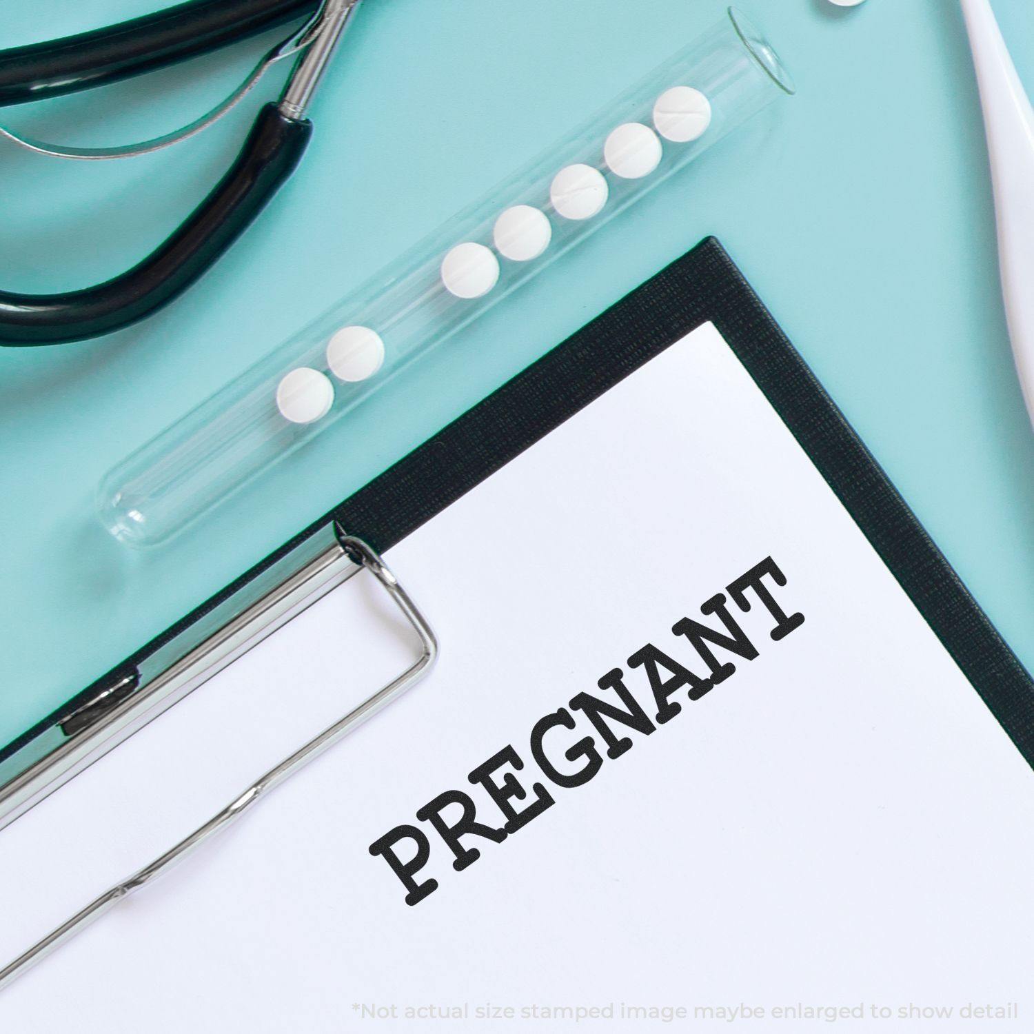 Clipboard with PREGNANT stamped on paper using Large Self Inking Pregnant Stamp, stethoscope, and pills in the background.