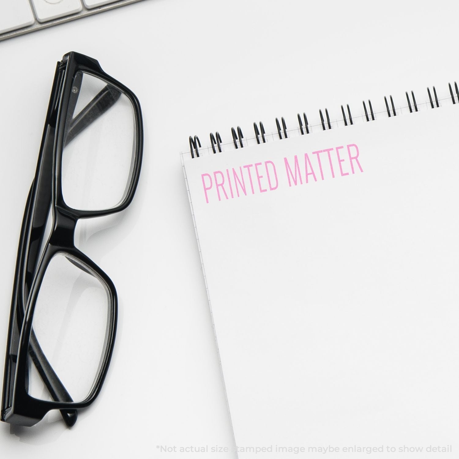 Self Inking Printed Matter Stamp used on a notebook next to black glasses and a keyboard.