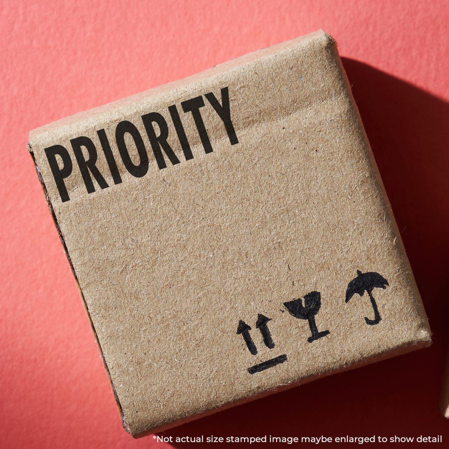 Cardboard box stamped with PRIORITY using the Large Pre-Inked Priority Stamp, placed on a red background.