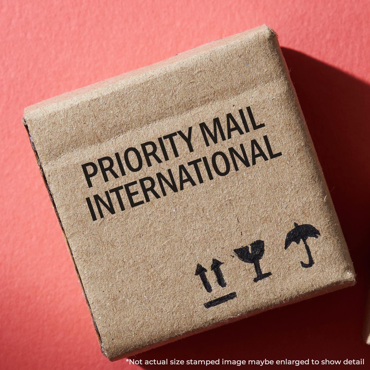 Large Self Inking Priority Mail International Stamp used on a brown cardboard box with shipping icons on a red background.