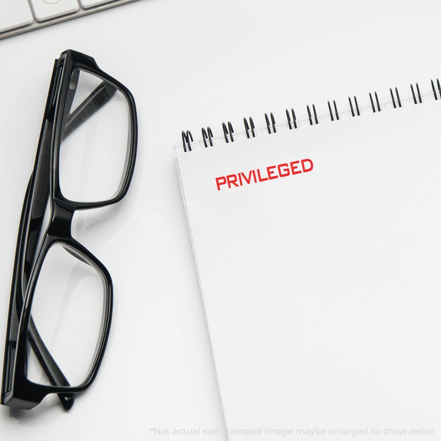 Privileged rubber stamp in red ink on a white notepad, next to black eyeglasses and a keyboard.