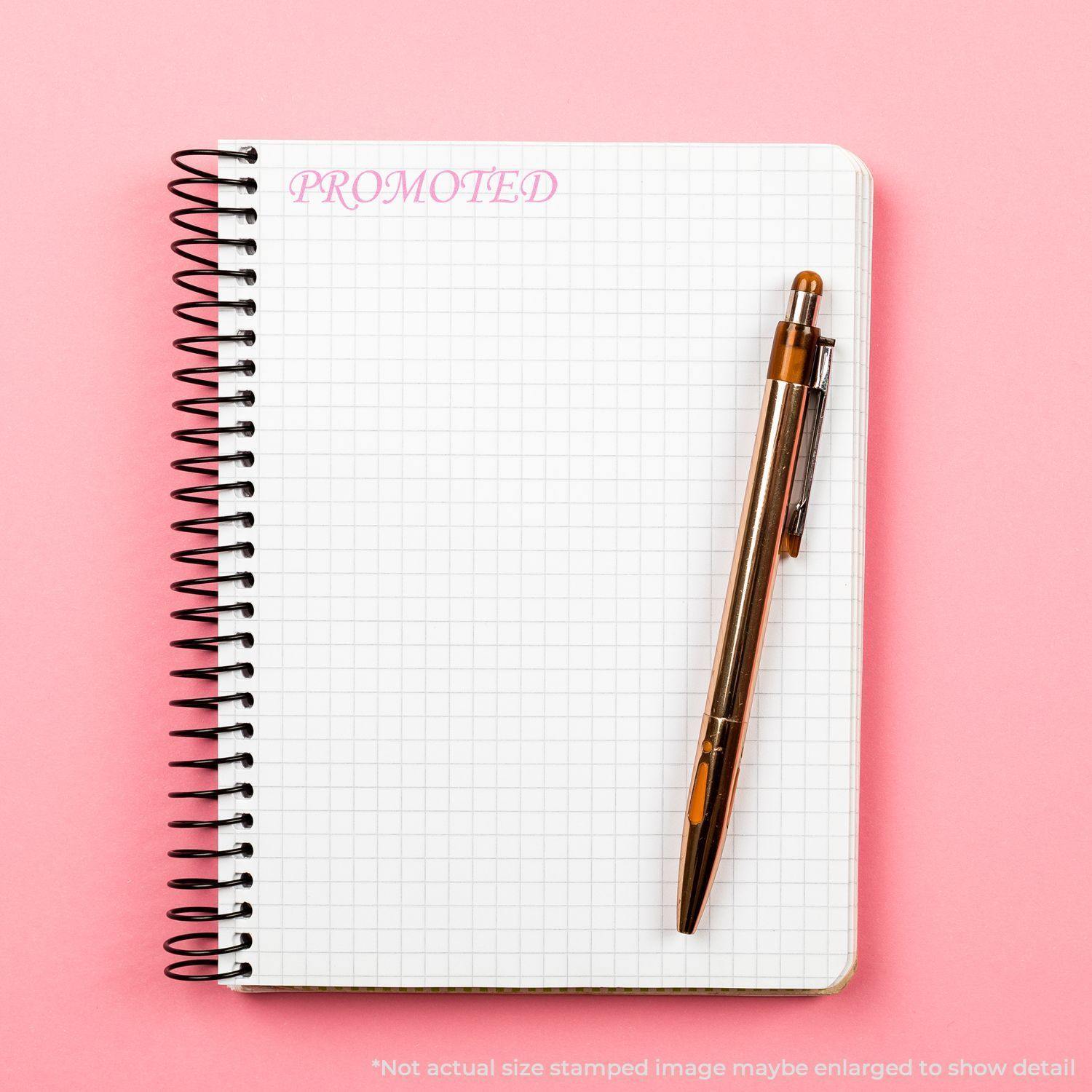 Large Self Inking Promoted Stamp imprint on a spiral notebook with a pen on a pink background.