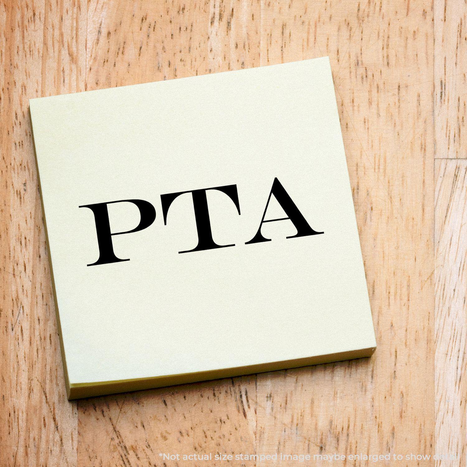 Slim Pre-Inked PTA Stamp on a yellow sticky note with PTA text, placed on a wooden surface.