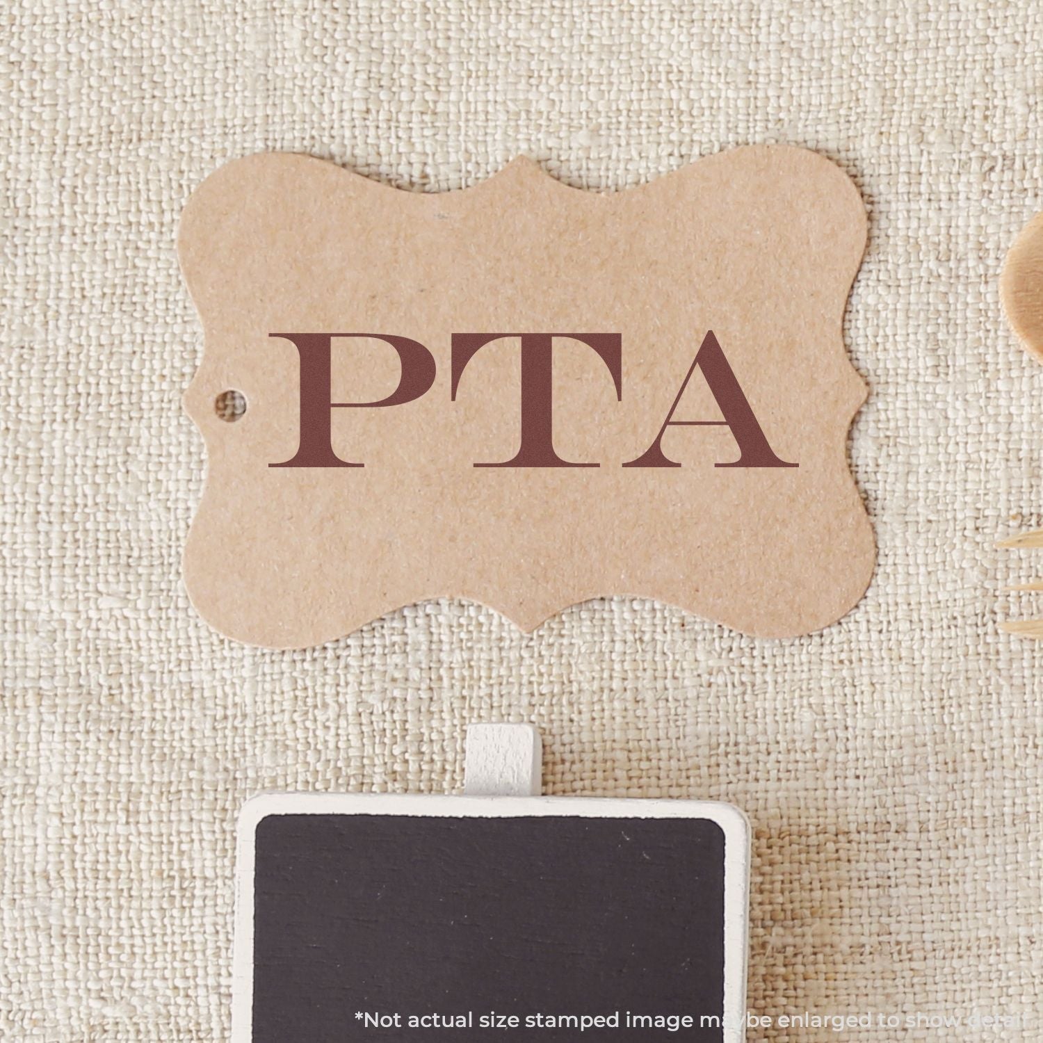 Self Inking PTA Stamp on a brown tag with PTA text, placed on a textured beige surface.