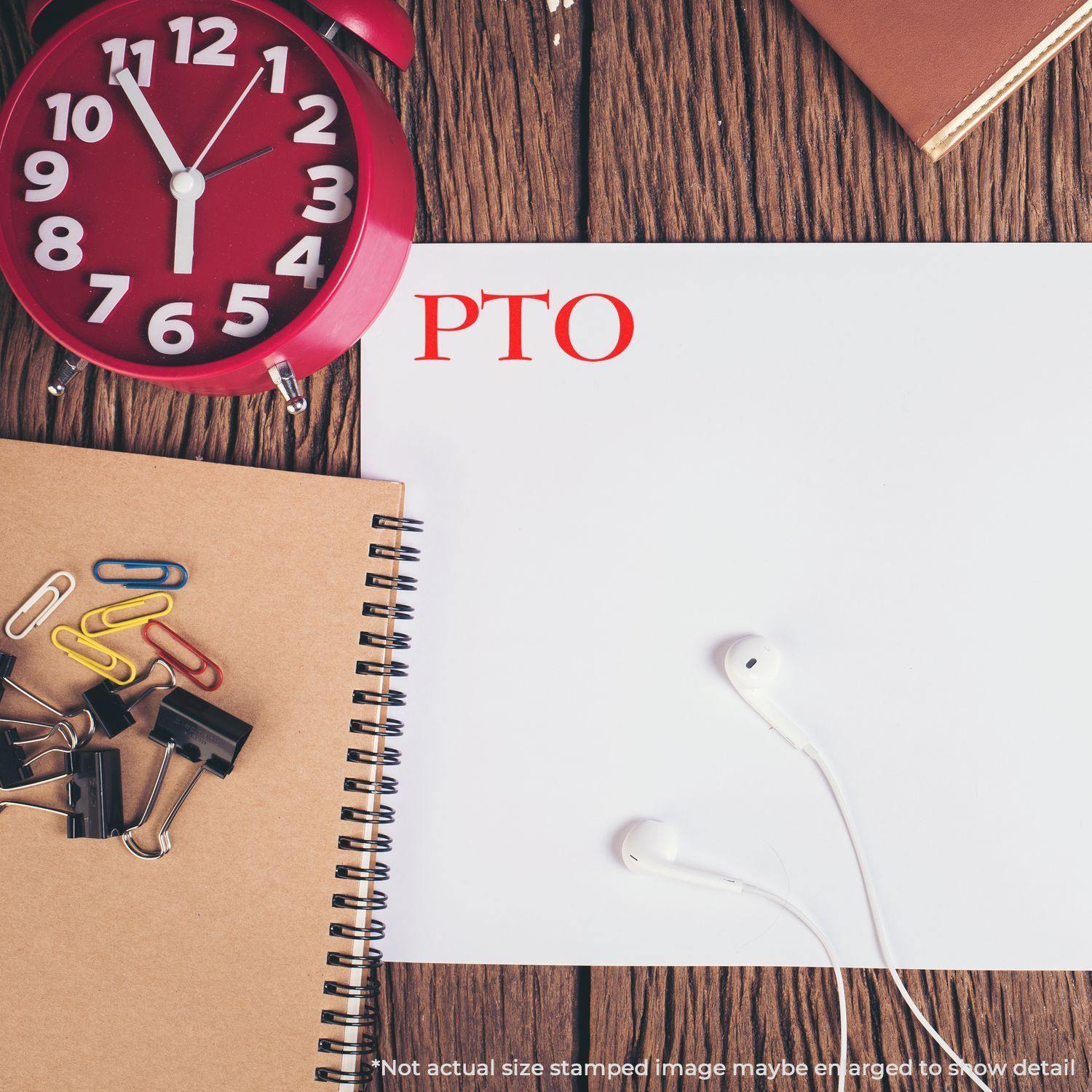 Desk with a red clock, notebooks, paper clips, earphones, and a white paper stamped with PTO in red using a PTO Rubber Stamp.