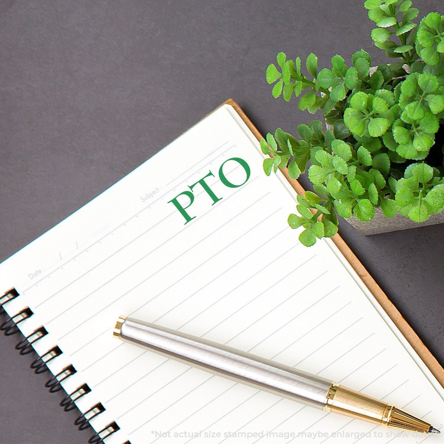 Self Inking PTO Stamp used on a notebook page next to a pen and a small potted plant on a gray surface.