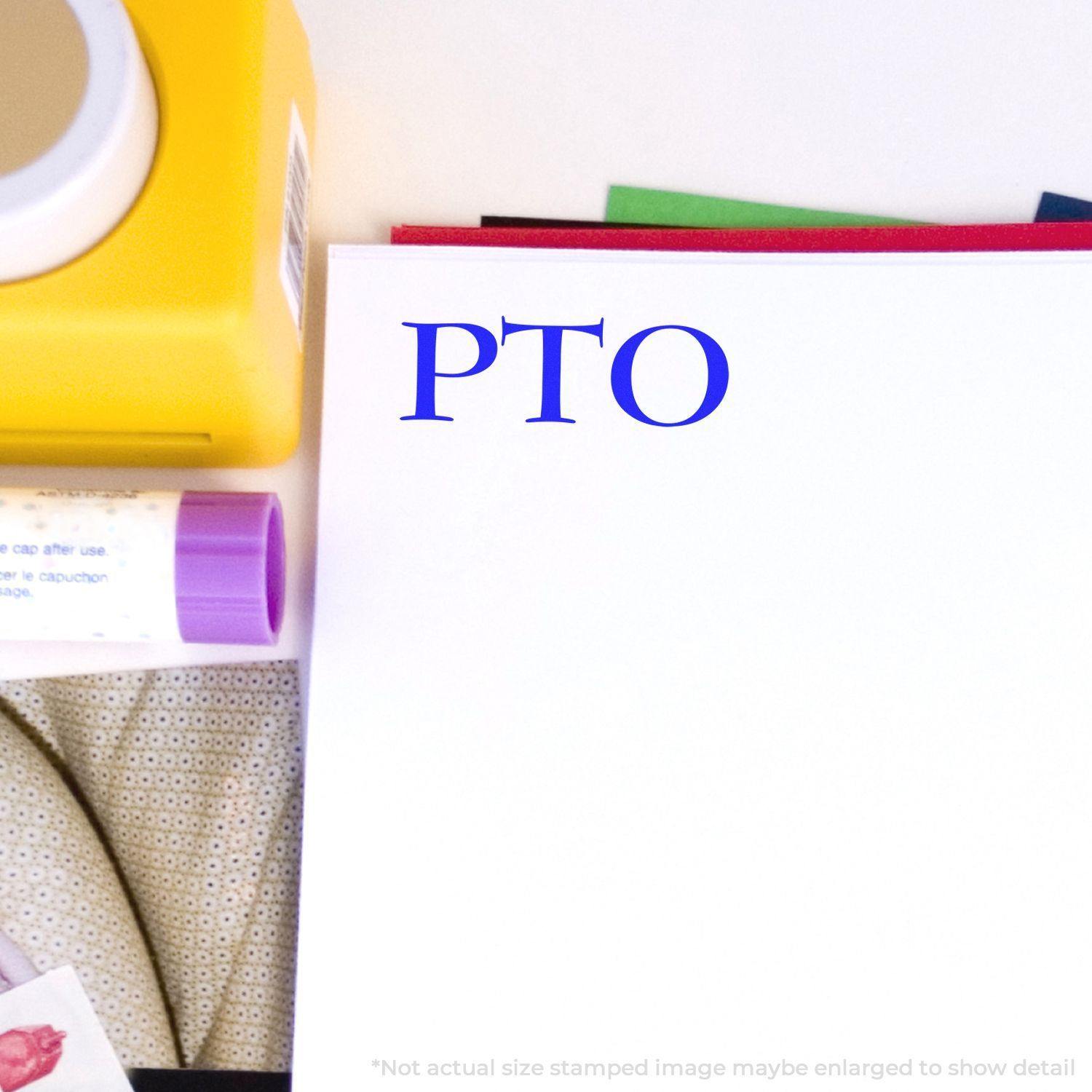 Slim Pre-Inked PTO Stamp in blue ink on white paper, surrounded by office supplies including a yellow container and a glue stick.