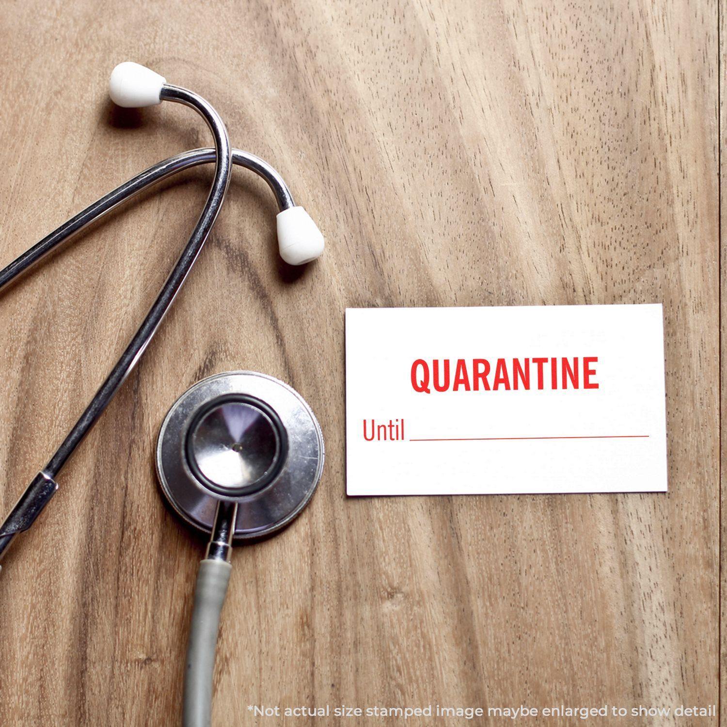 Slim Pre-Inked Quarantine Until Stamp on a card next to a stethoscope on a wooden surface.