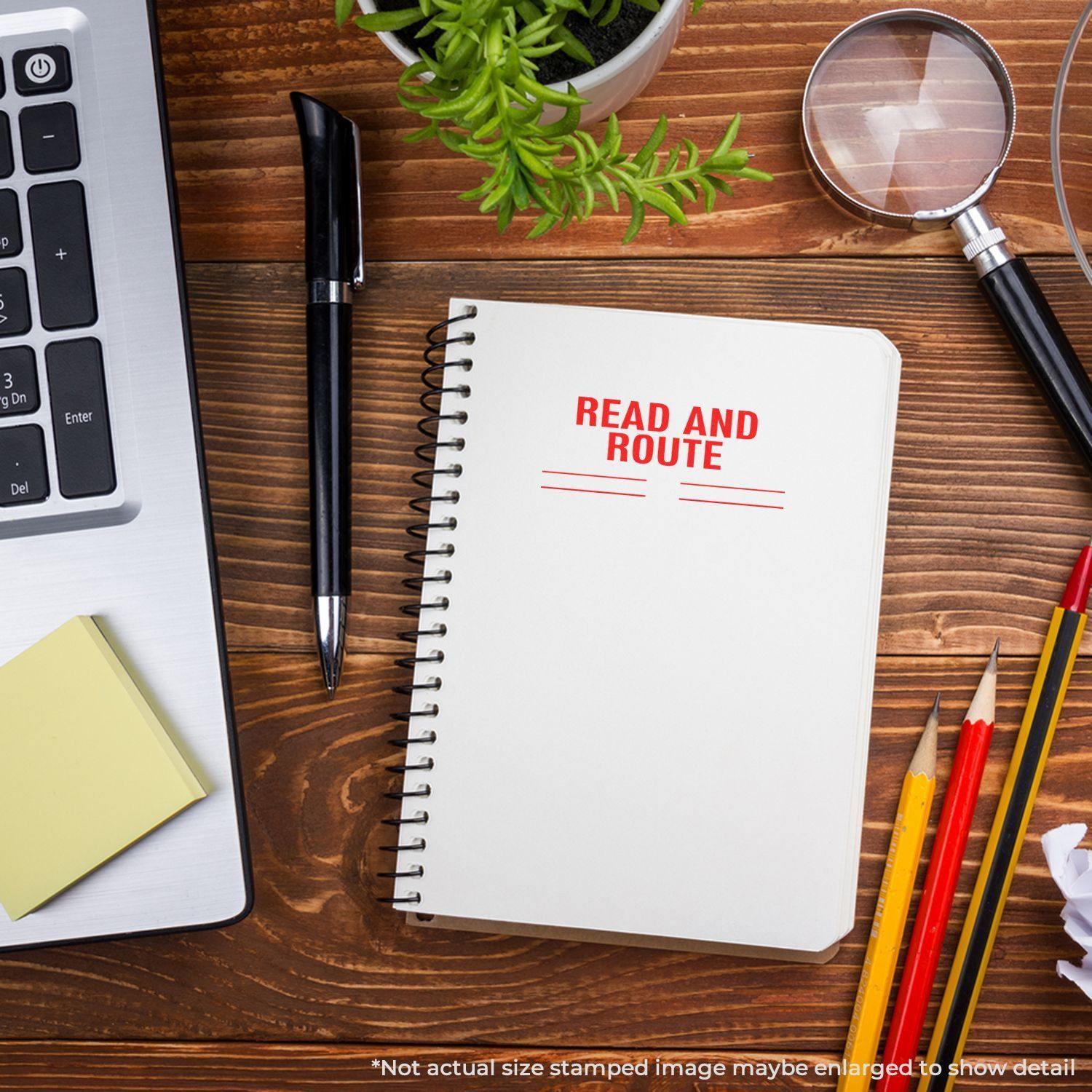 Desk with laptop, pen, sticky notes, magnifying glass, pencils, plant, and notebook stamped with 'Read and Route' in red.