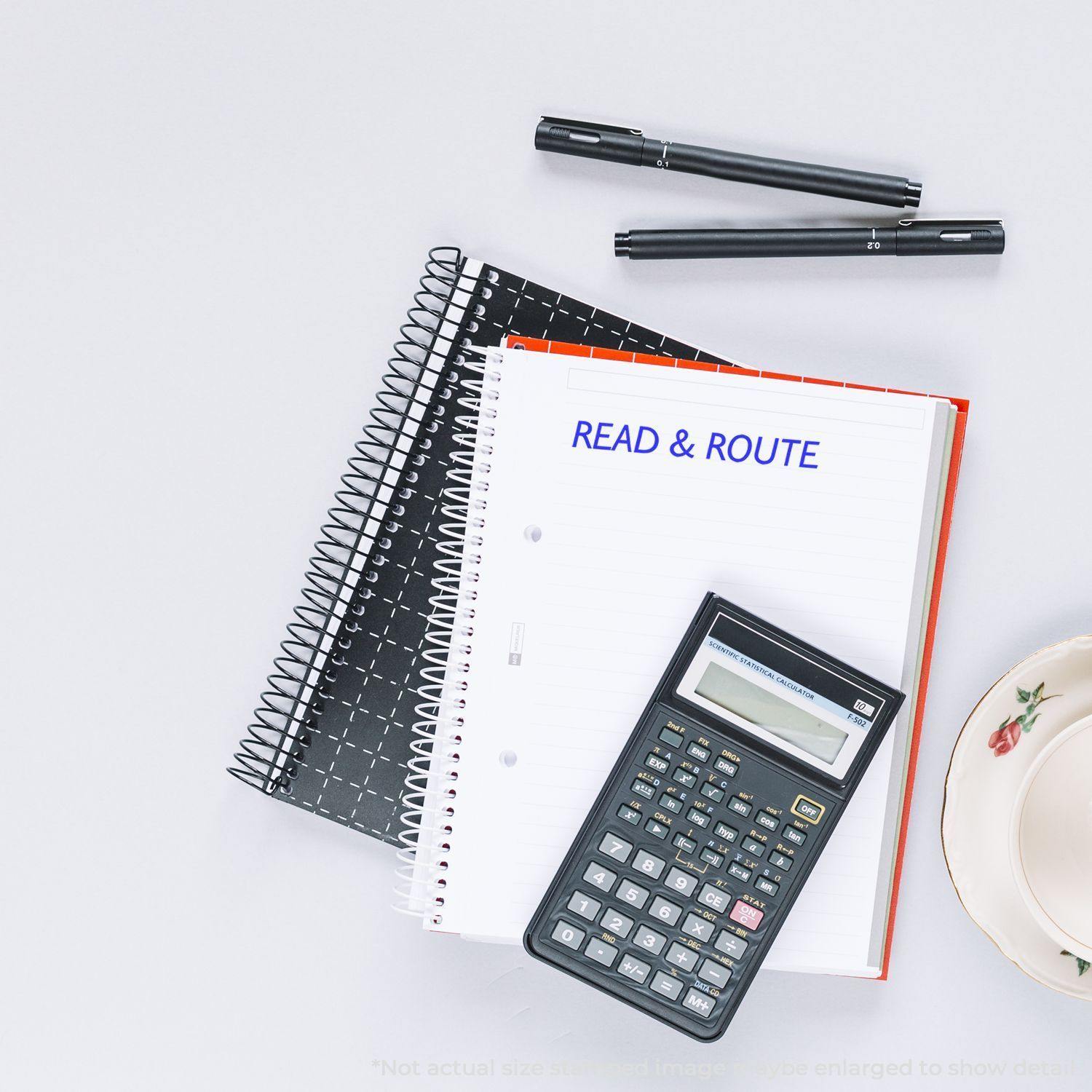 Desk with notebooks, calculator, pens, and a Read & Route Rubber Stamp impression on a notebook page.