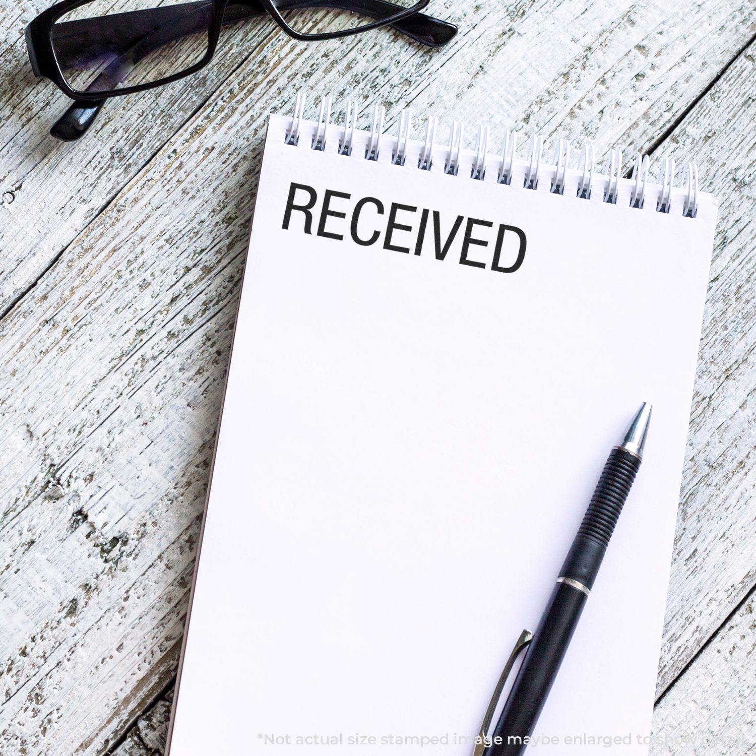 Notebook with "RECEIVED" stamped on a page, pen, and glasses on a wooden surface. Product: Received Rubber Stamp.