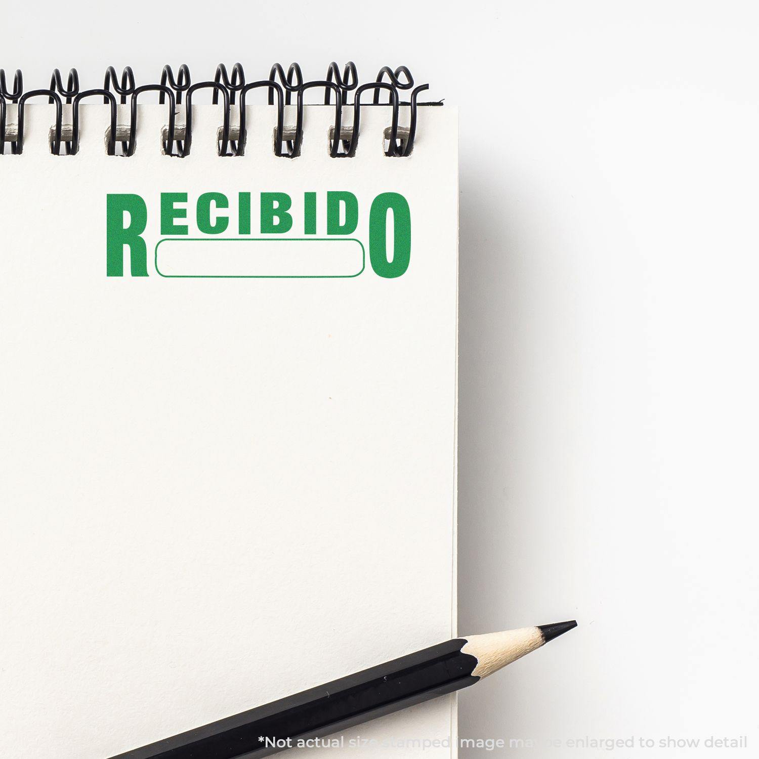 A notebook with a Recibido rubber stamp impression in green ink, accompanied by a black pencil on a white background.