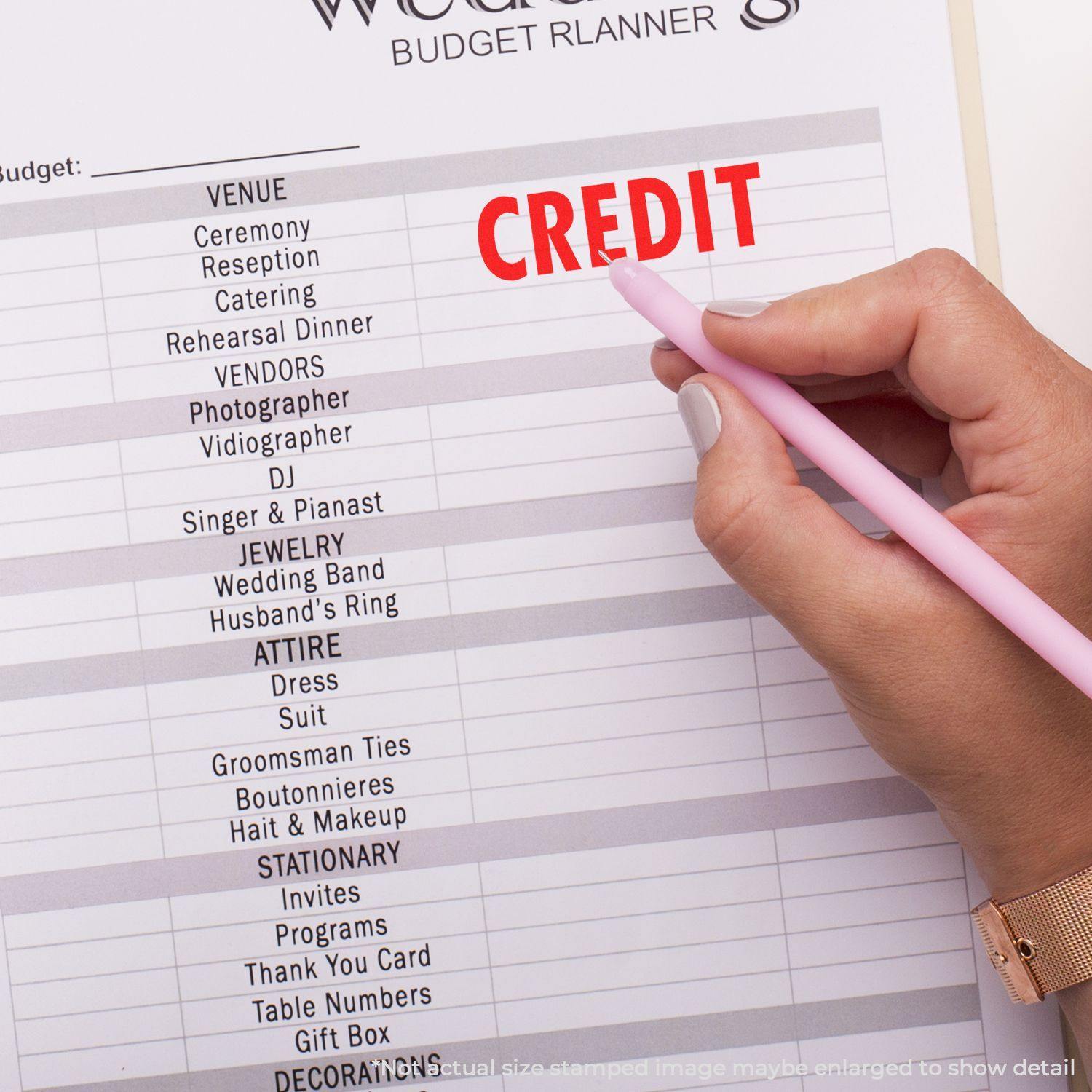 A hand using the Self Inking Credit Stamp to mark CREDIT in red on a budget planner.