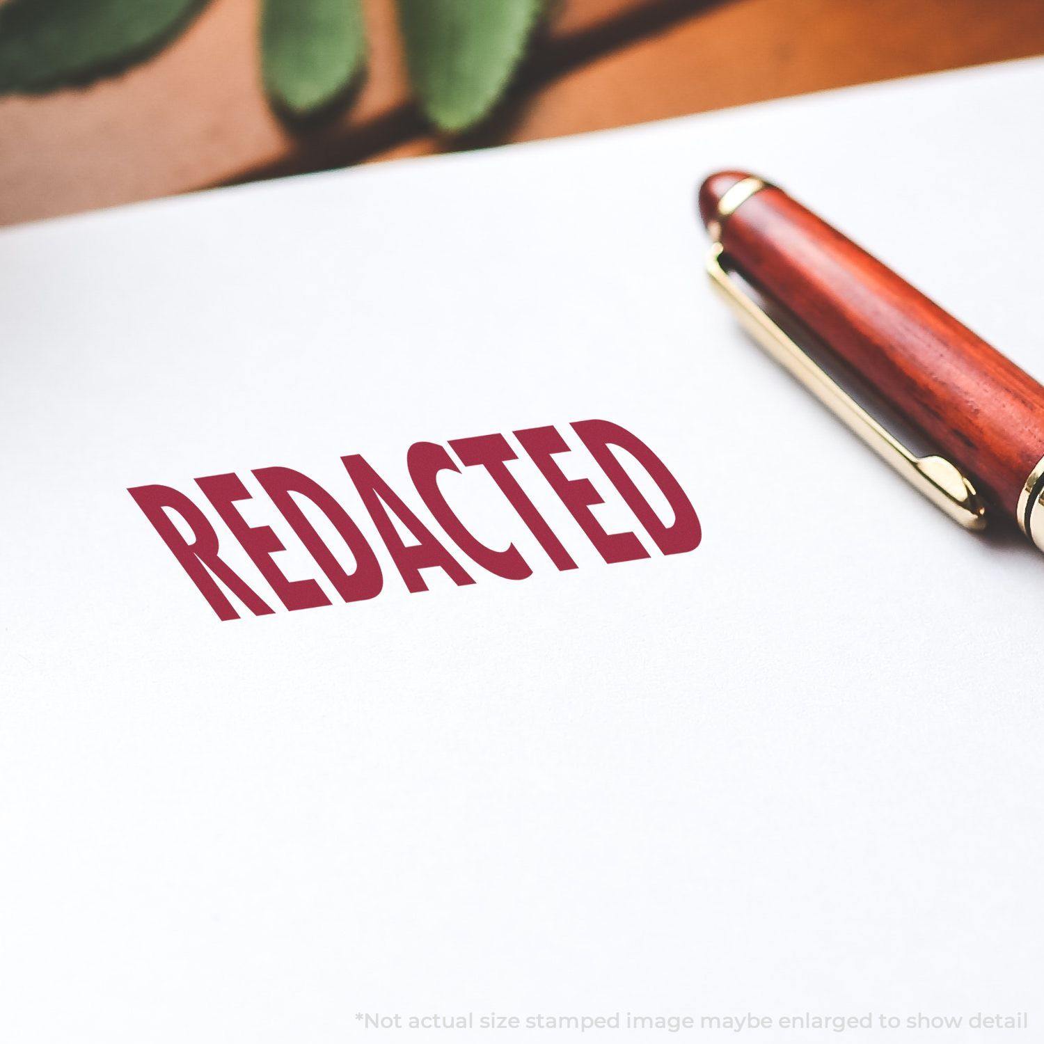 Large Self Inking Redacted Stamp used on white paper with a redacted mark, next to a wooden pen.