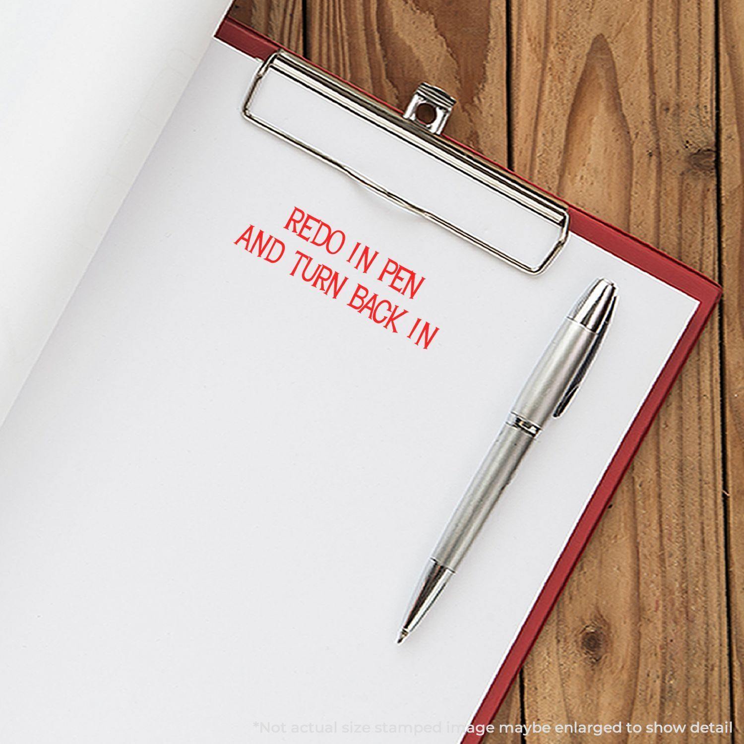 Clipboard with paper stamped Redo In Pen And Turn Back In in red ink, next to a silver pen on a wooden surface.