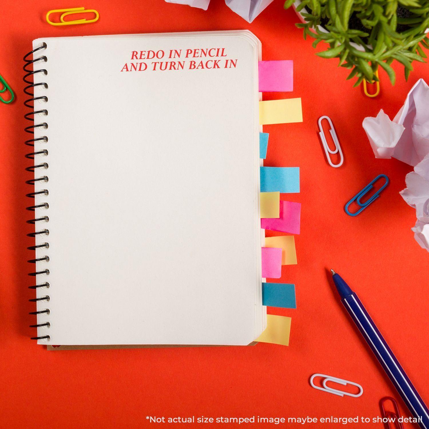 A notebook with colorful tabs and the Large Redo In Pencil And Turn Back In Rubber Stamp imprint on a red background with office supplies.