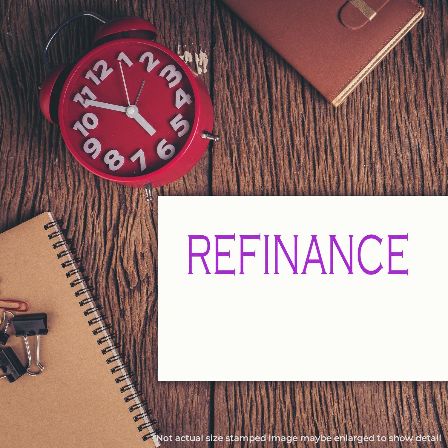 Large Pre-Inked Refinance Stamp used on a white card, placed on a wooden desk with a red clock, notebook, and office supplies.