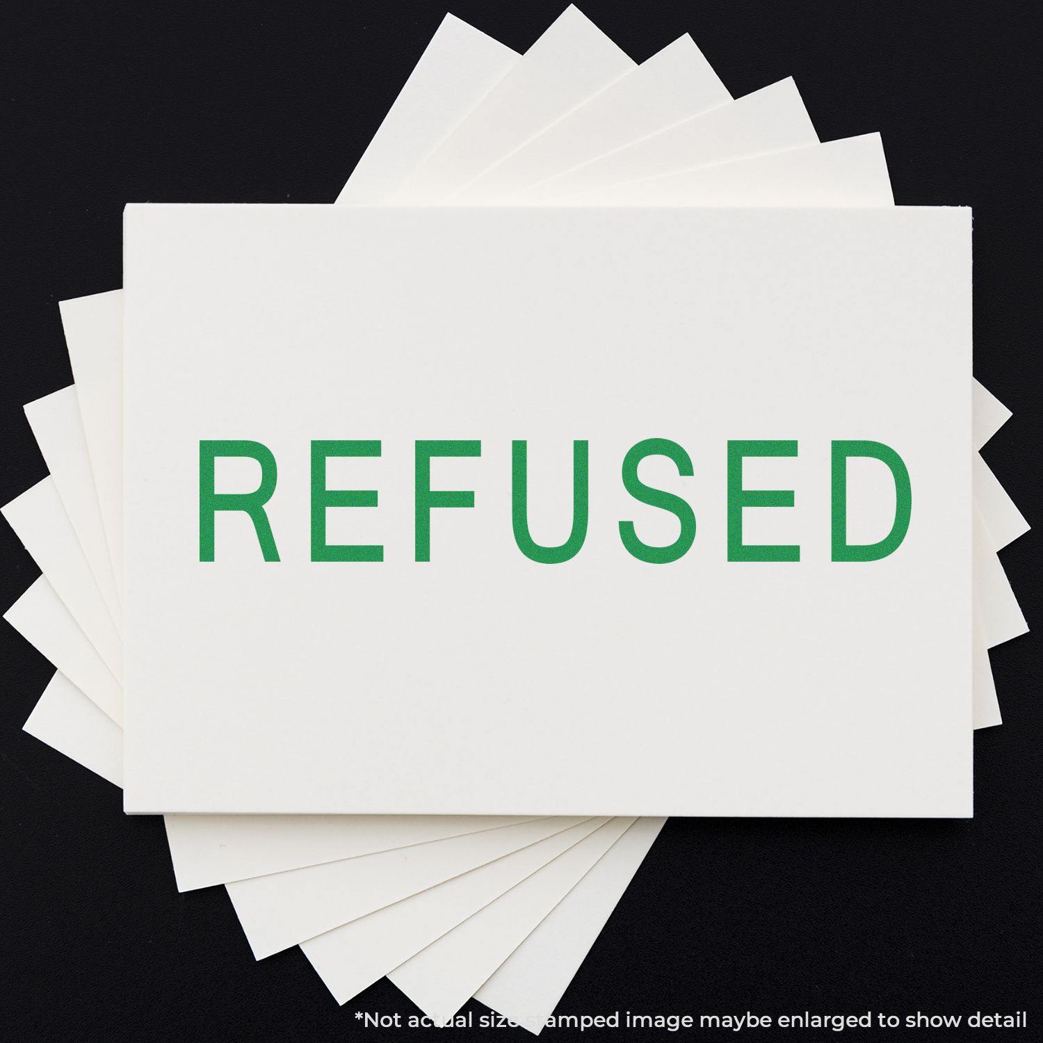 Large Self Inking Refused Stamp in green ink on white paper, with multiple sheets fanned out underneath on a black background.