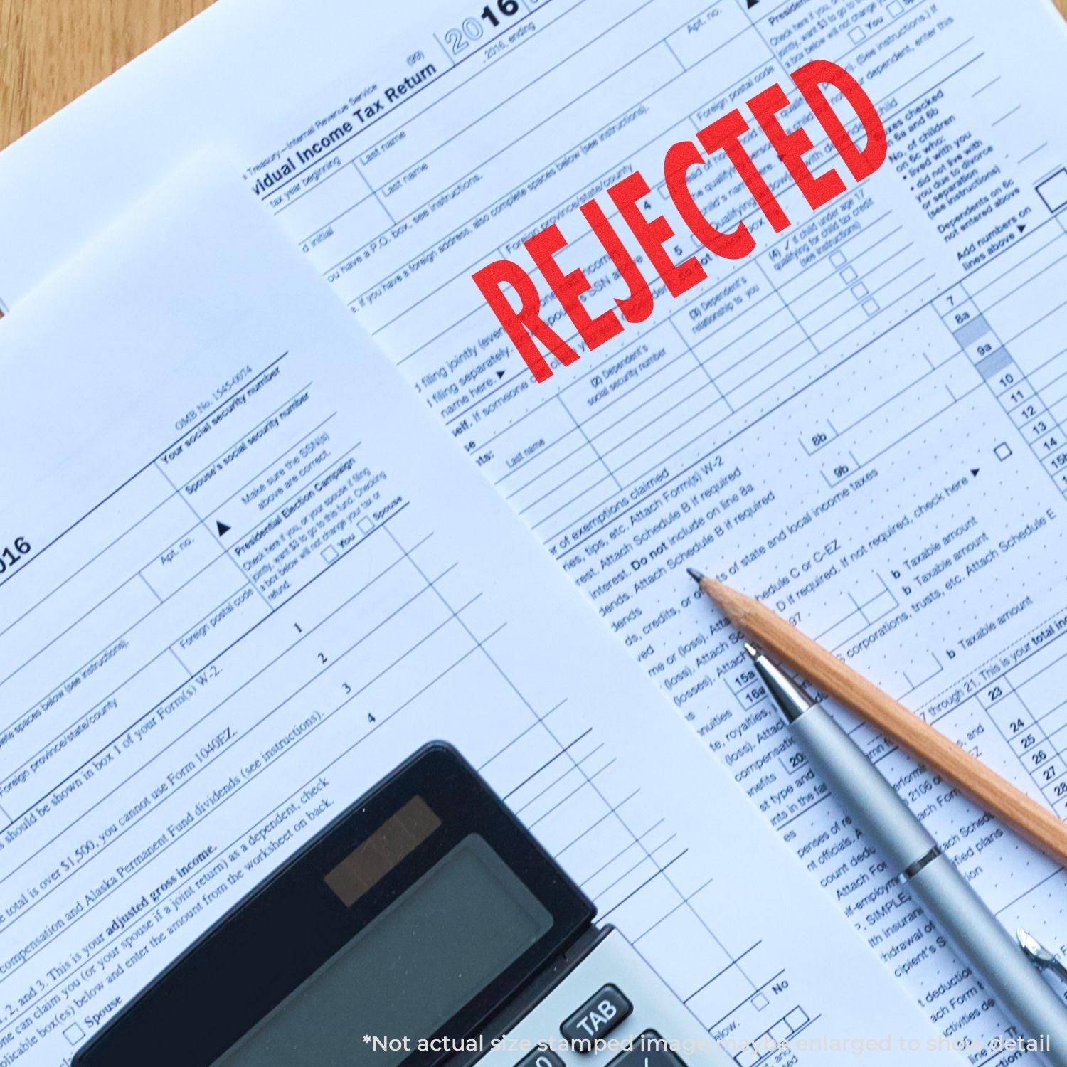 A Self Inking Rejected Stamp marks a tax return form with REJECTED in red ink, next to a calculator and pencil on a desk.