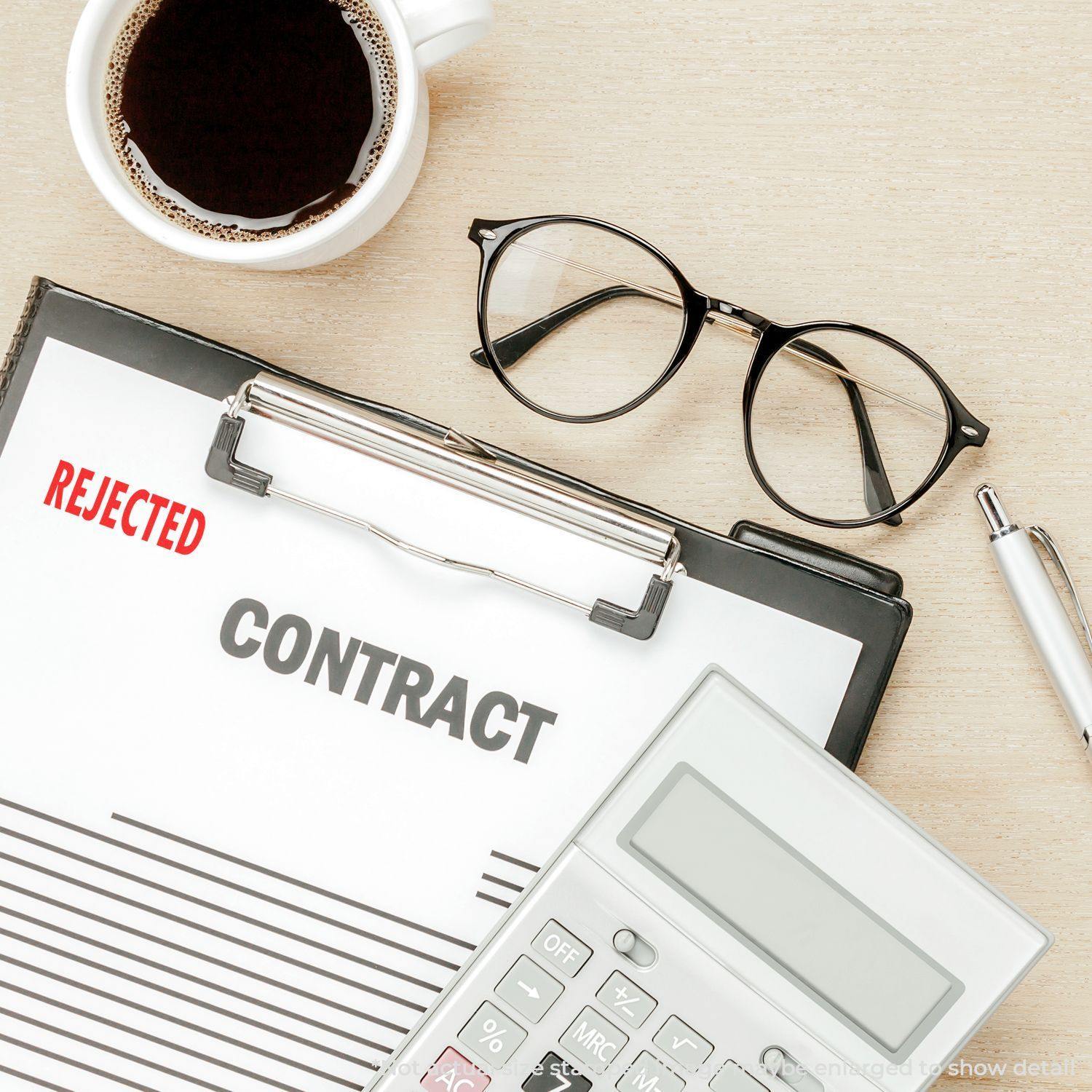 Large Self Inking Rejected Stamp used on a contract document on a clipboard, with a calculator, glasses, pen, and coffee cup nearby.