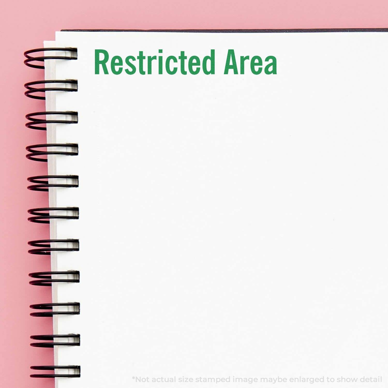 Restricted Area Rubber Stamp impression on a white spiral notebook with a pink background.