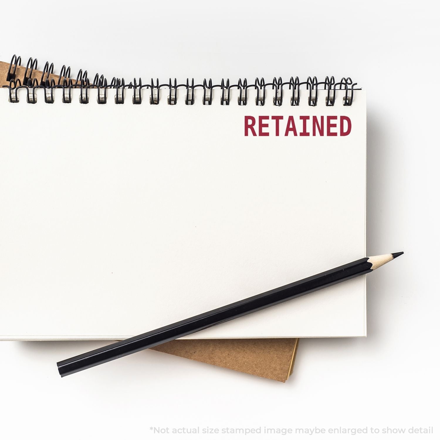 Self Inking Retained Stamp marking RETAINED in red on a white notebook page, with a black pencil placed beside it.