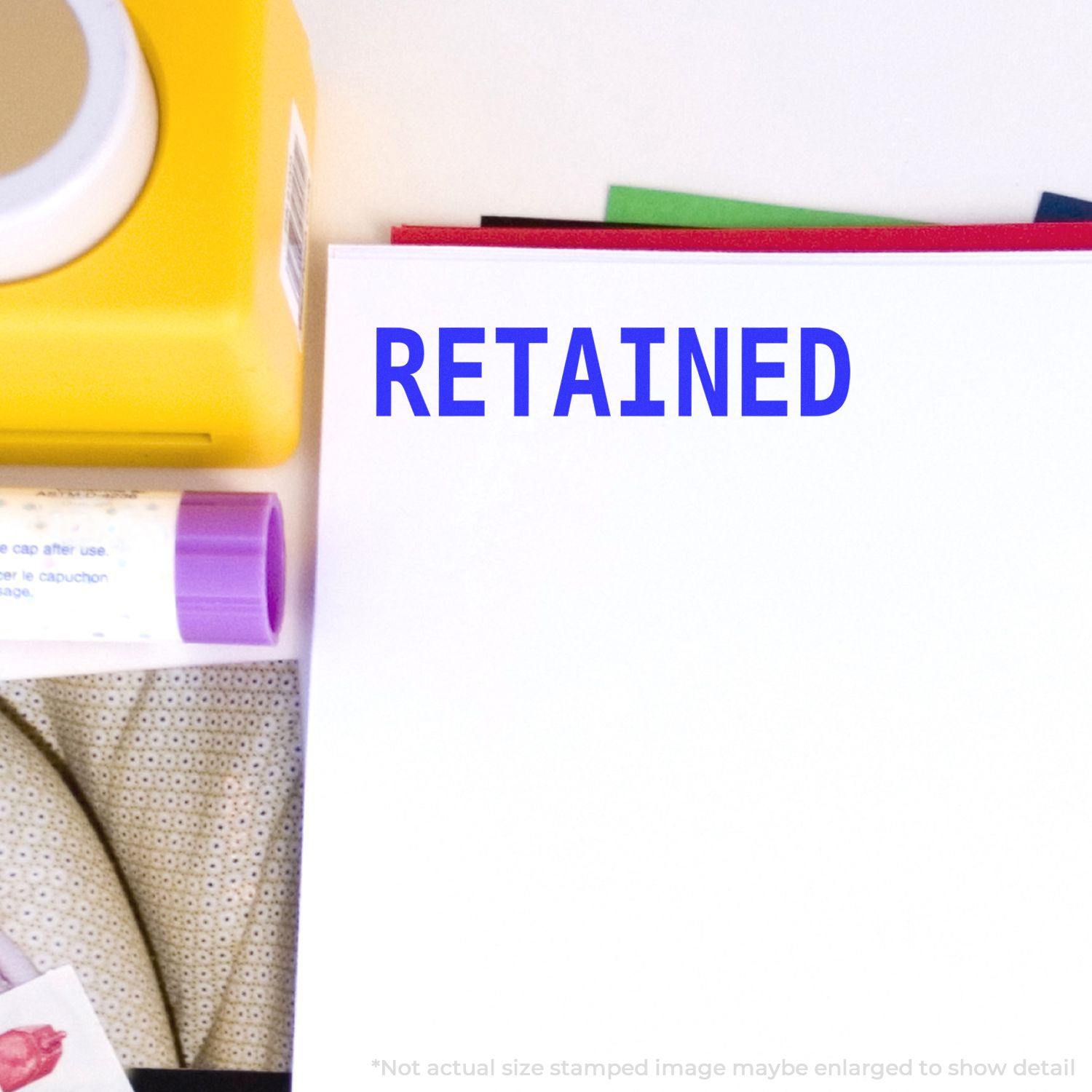 Retained rubber stamp impression on white paper, with office supplies including a yellow stamp pad and glue stick nearby.