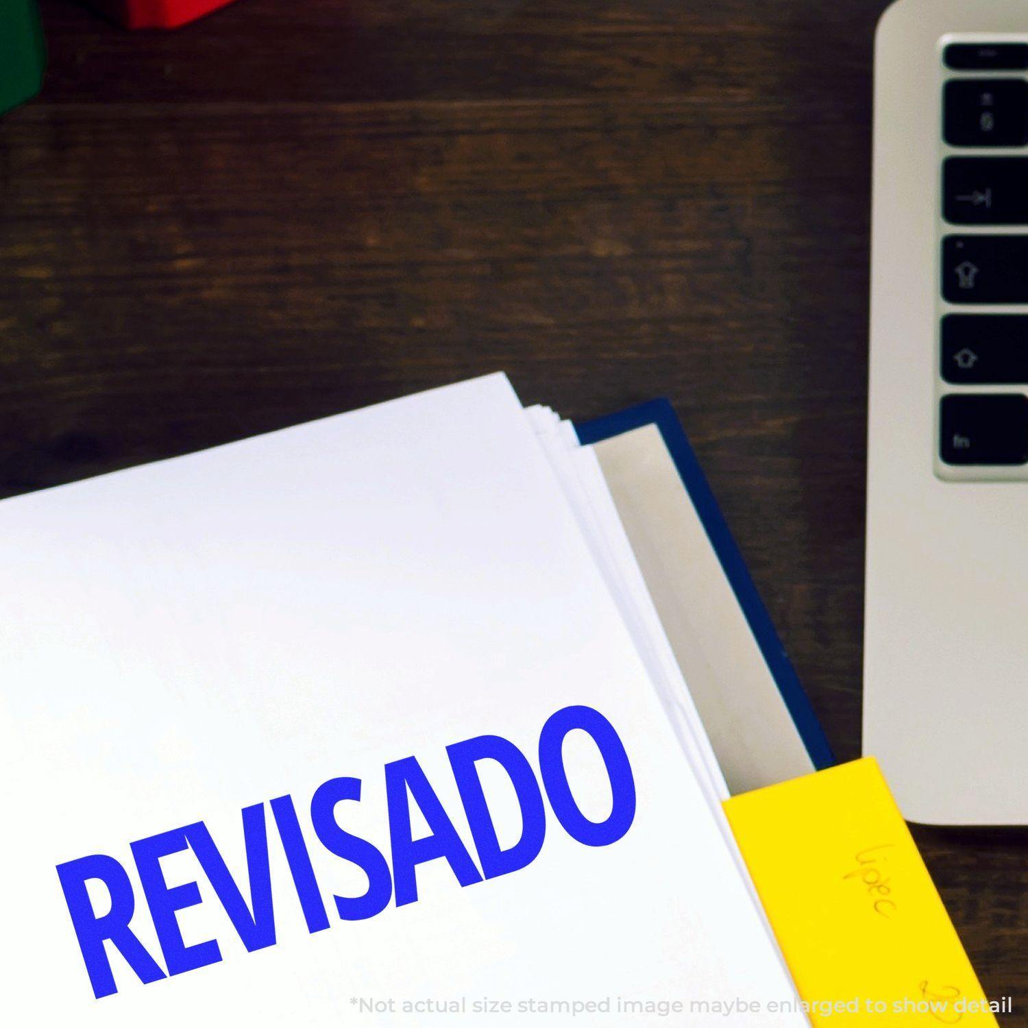 Slim Pre-Inked Revisado Stamp marking a document on a desk next to a laptop and a yellow sticky note.