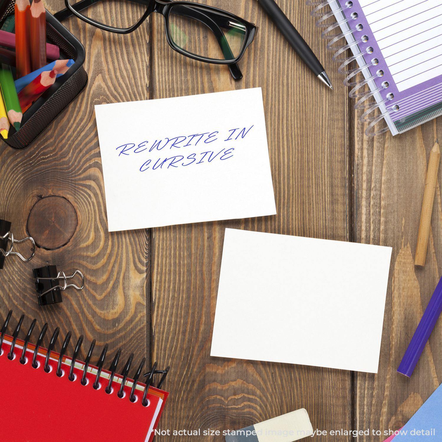 Large Pre-Inked Rewrite In Cursive Stamp used on a white card, surrounded by office supplies on a wooden desk.