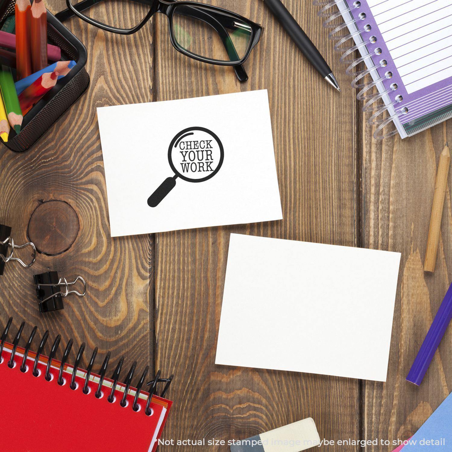 Round Check Your Work rubber stamp on a white card, surrounded by office supplies like notebooks, glasses, and pens on a wooden desk.