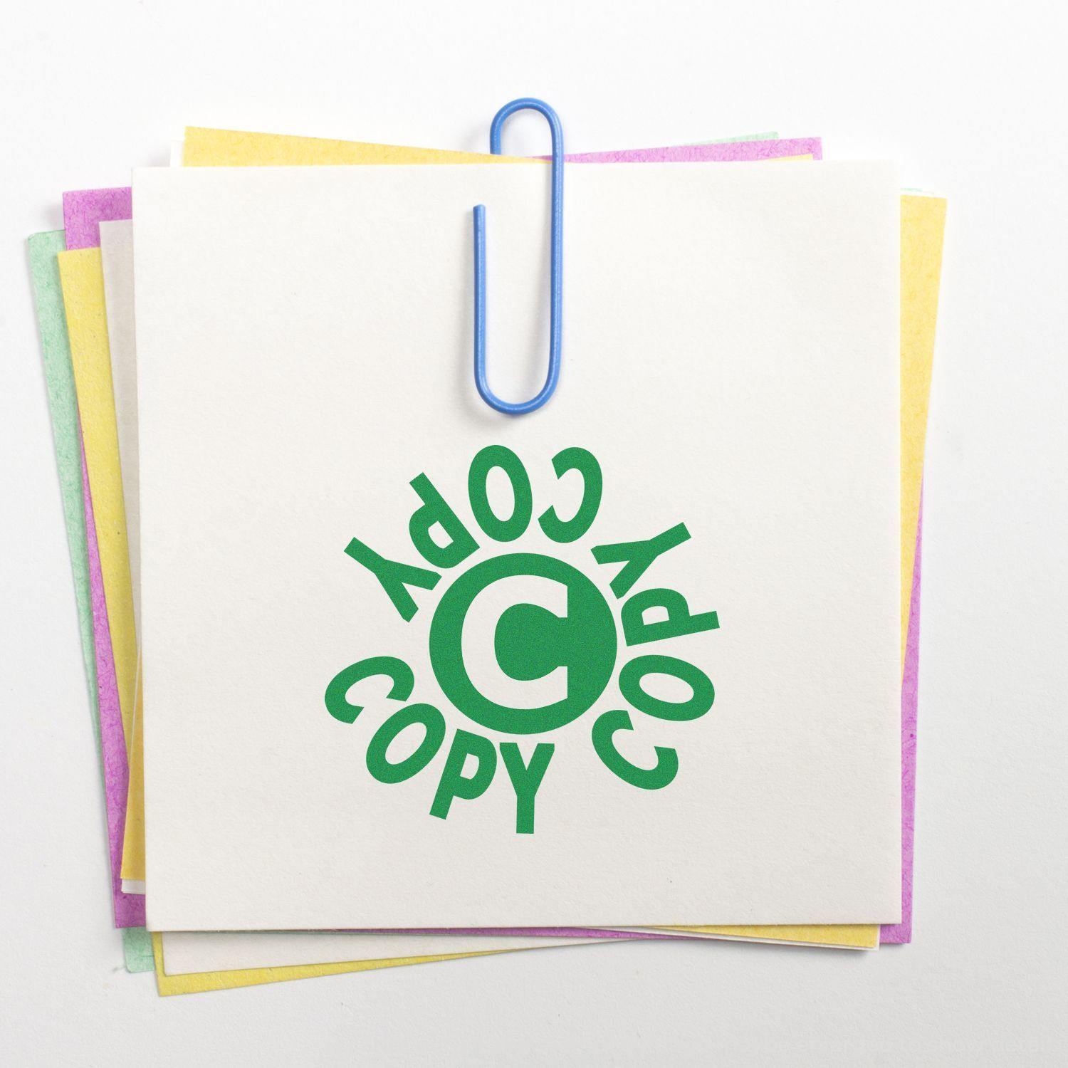 A stack of colorful papers with a blue paperclip and a green Round Copy Copy Copy Rubber Stamp imprint on the top paper.