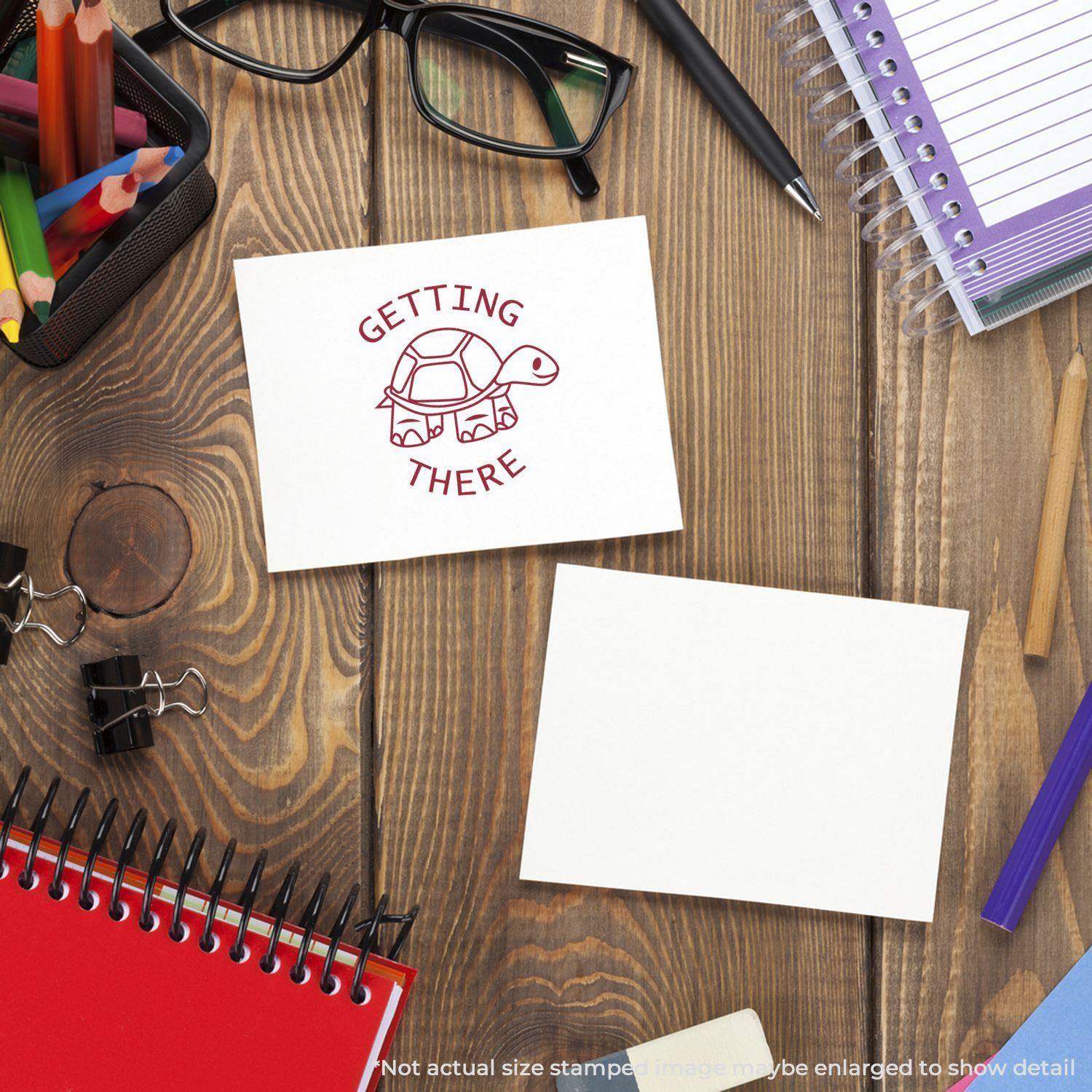 Round Getting There Rubber Stamp on a card with a turtle design, surrounded by office supplies on a wooden desk.