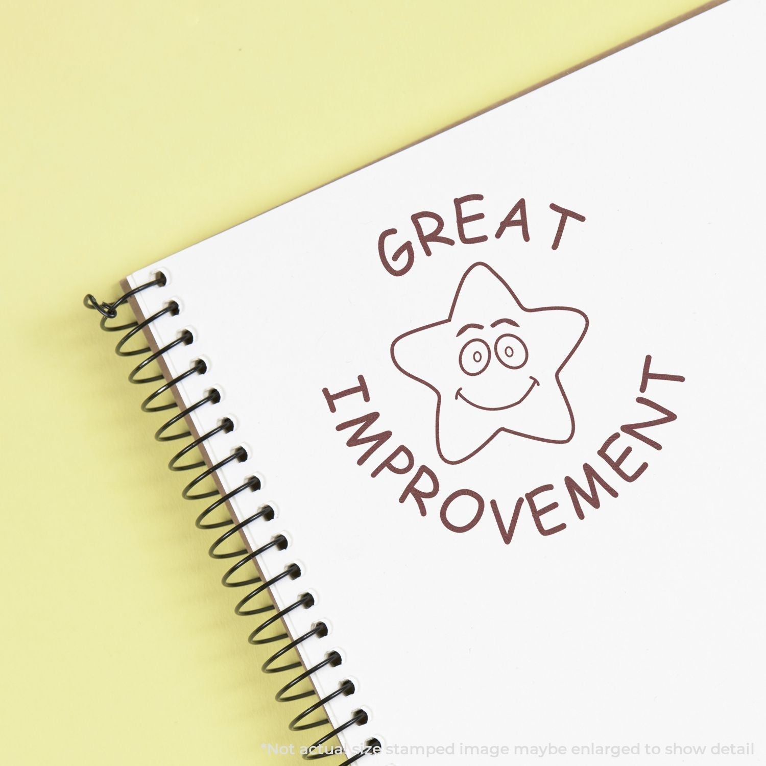 A Self Inking Round Great Improvement Stamp imprint on a spiral notebook, featuring a smiling star and the words GREAT IMPROVEMENT in brown ink.