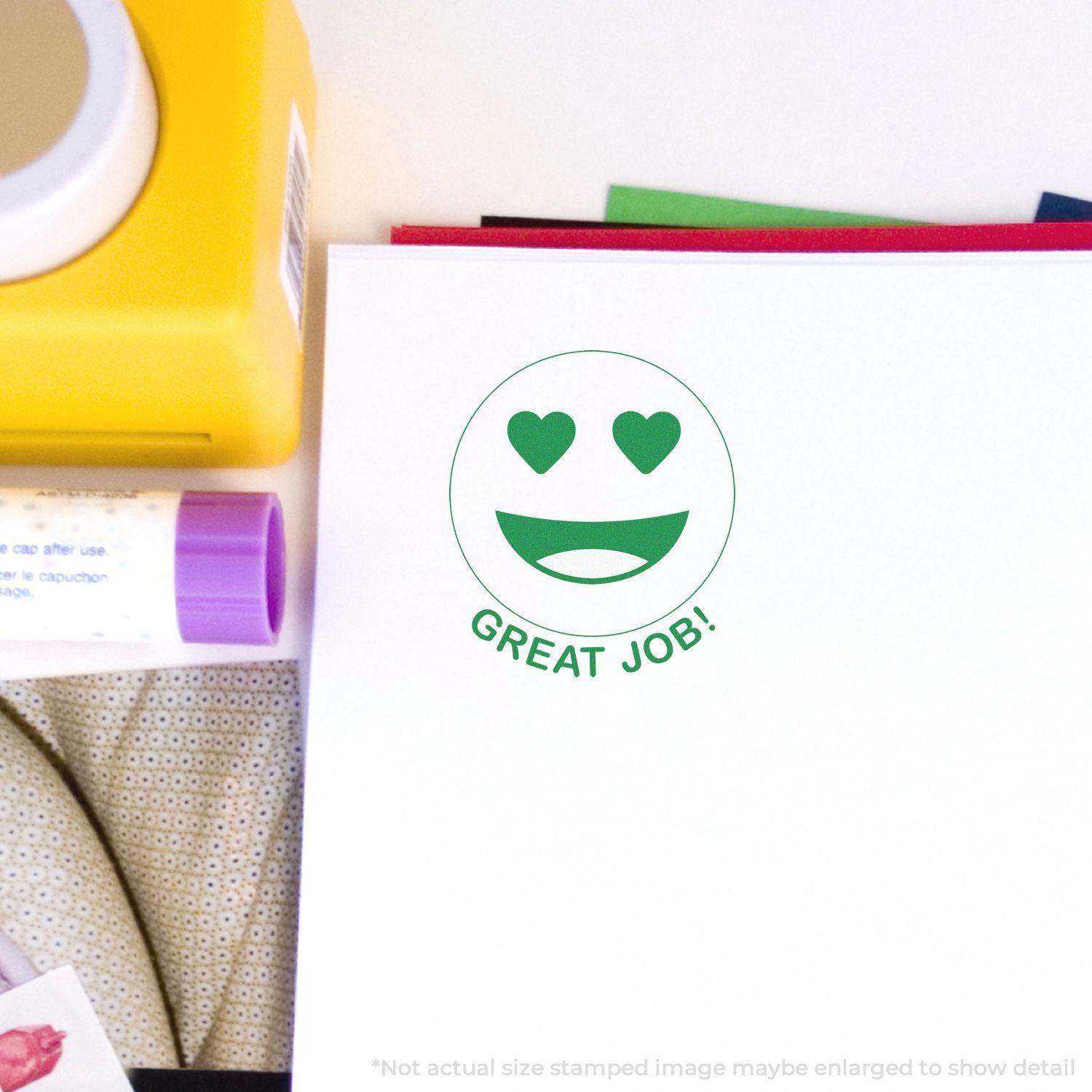 Round Great Job Smiley Rubber Stamp with heart eyes and a smiling mouth stamped in green ink on white paper, surrounded by stationery.