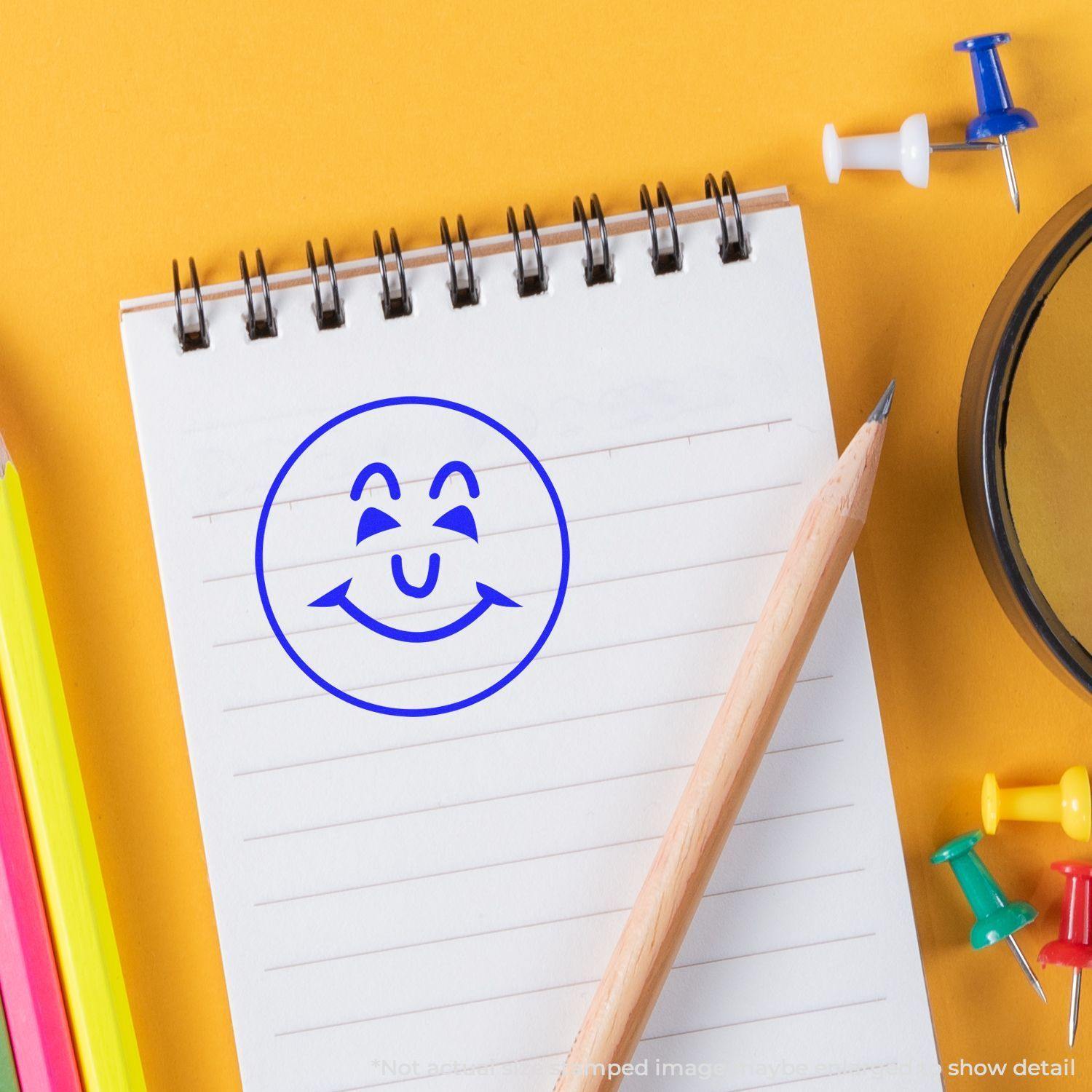 Round Happy Face Rubber Stamp on a notepad with a pencil, colorful push pins, and a magnifying glass on a yellow background.