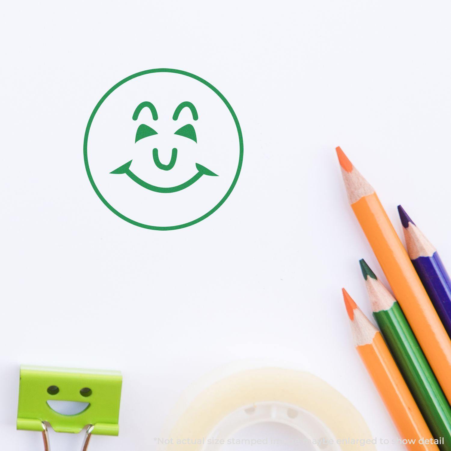 Round Happy Face Rubber Stamp impression in green ink on white paper, with colored pencils, tape, and a smiling clip nearby.